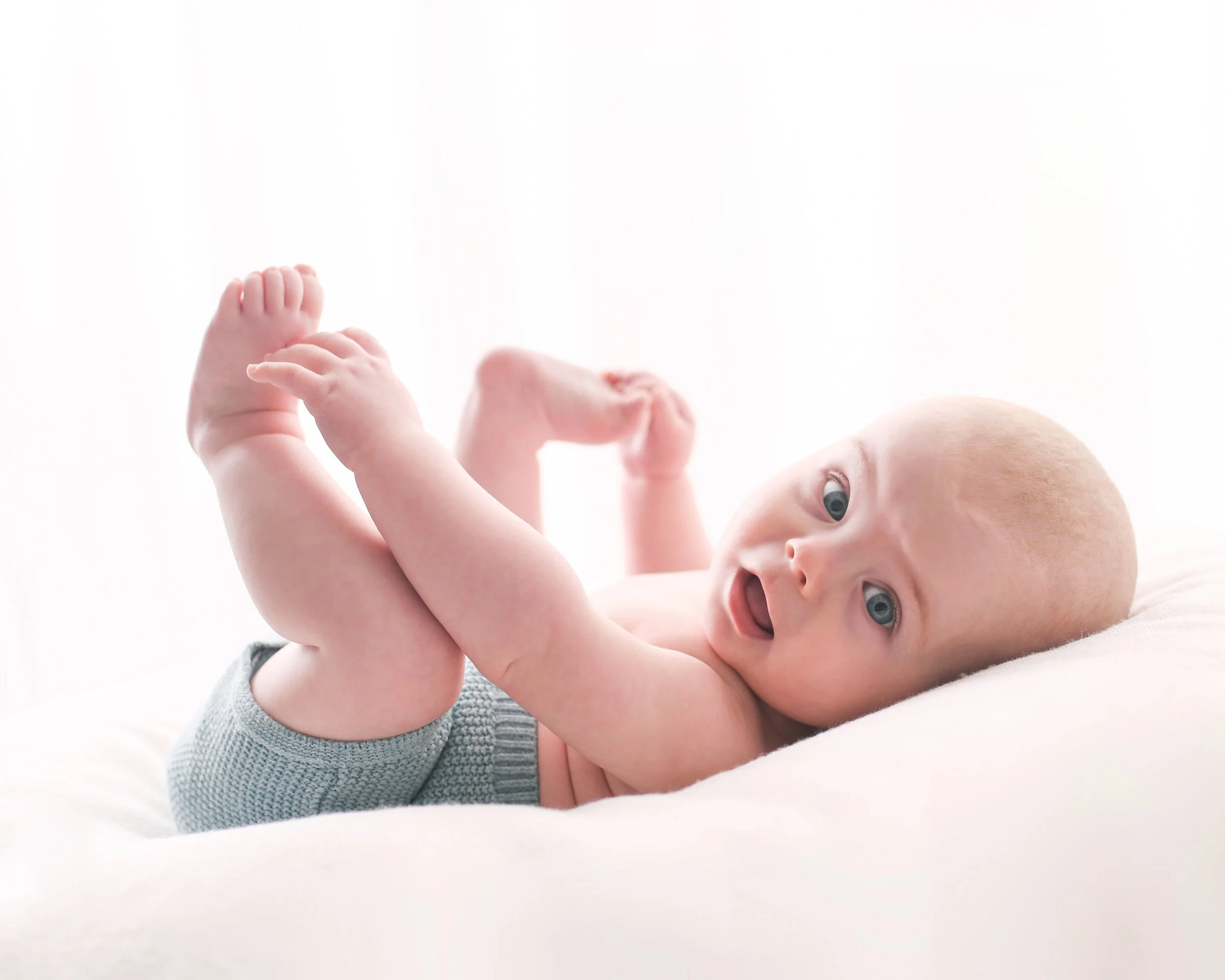 Baby looking at the camera holding their feet. Milestone photoshoot as baby is growing up