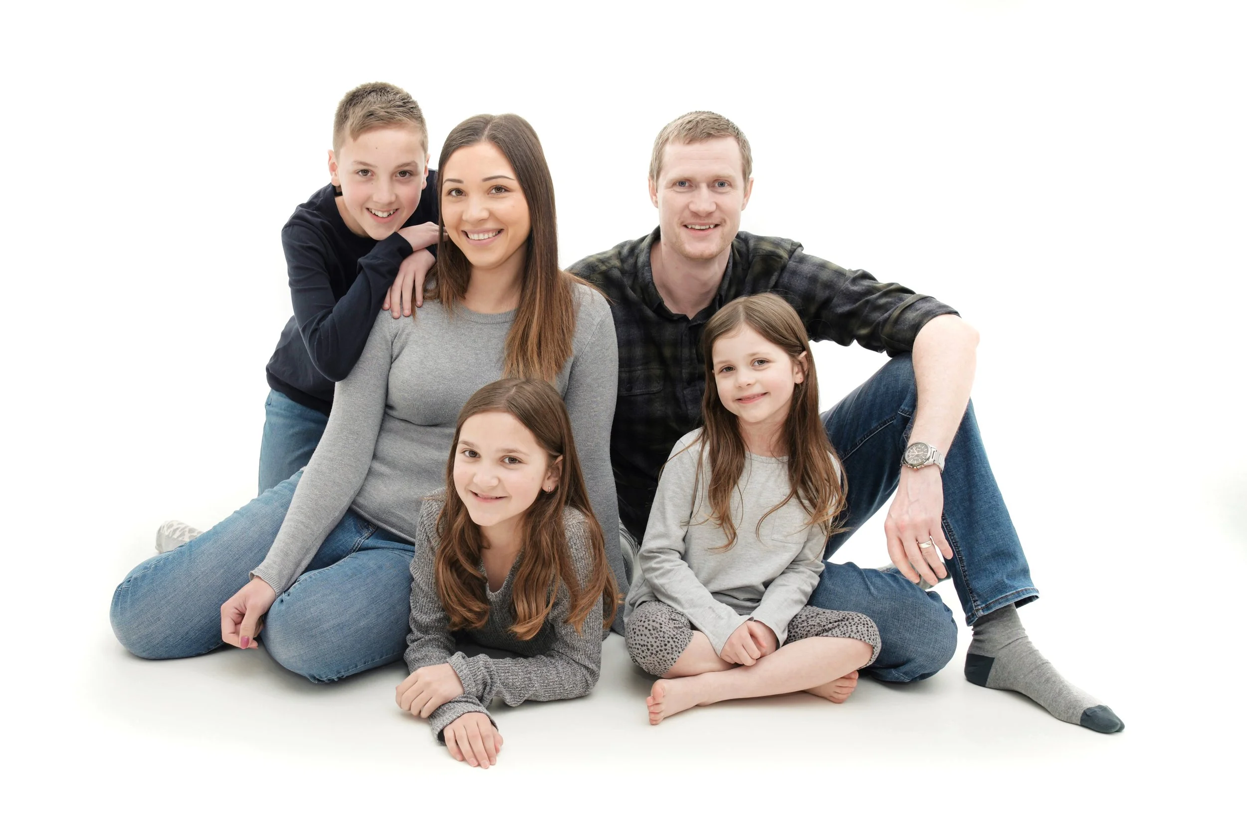 Family photoshoot in Warwickshire, Family of six, including three children and two adults, sitting and lying on a white background, smiling at the camera.