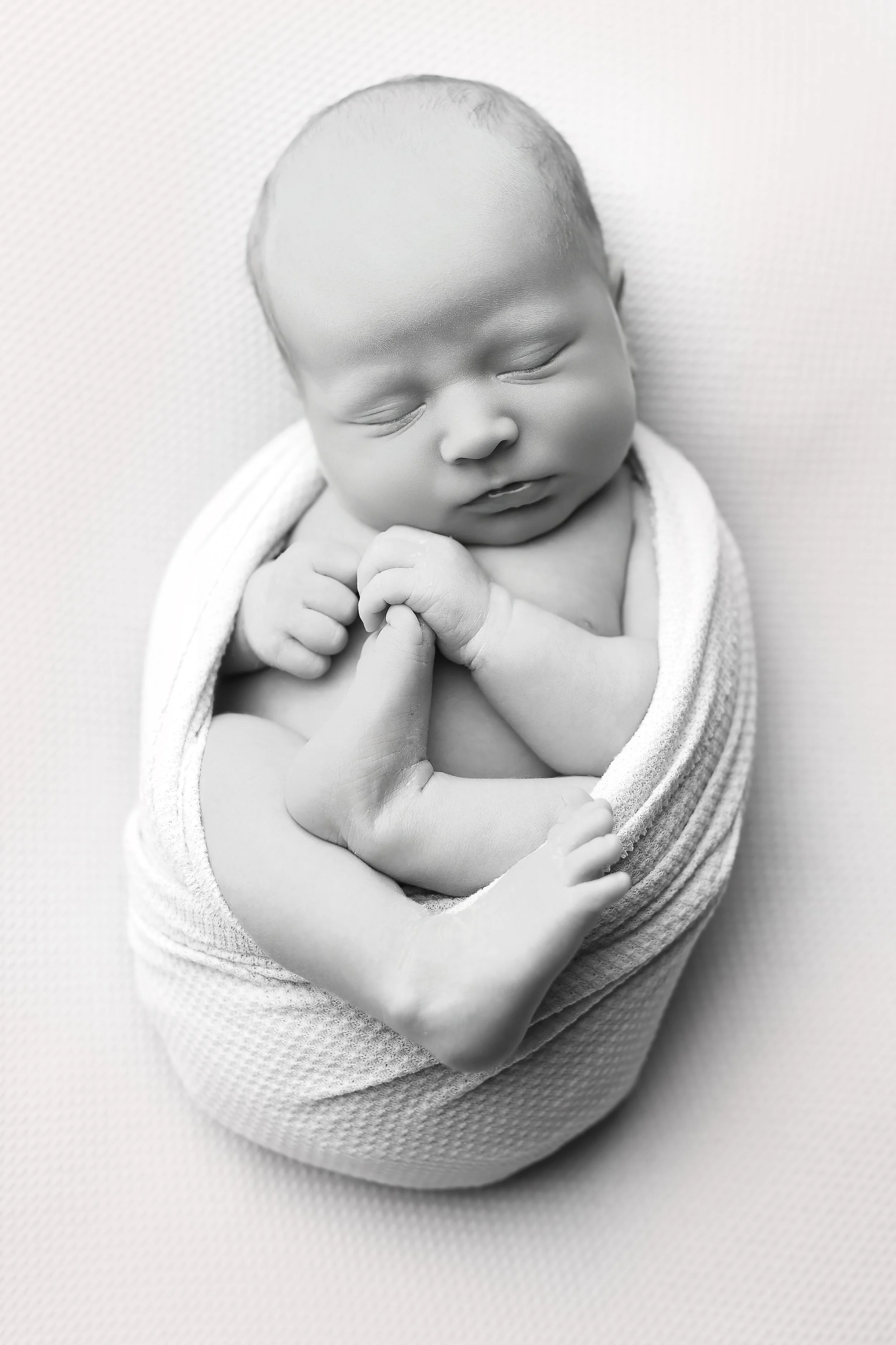 Baby holding their foot in the womb wrap. 2 weeks newborn photoshoot