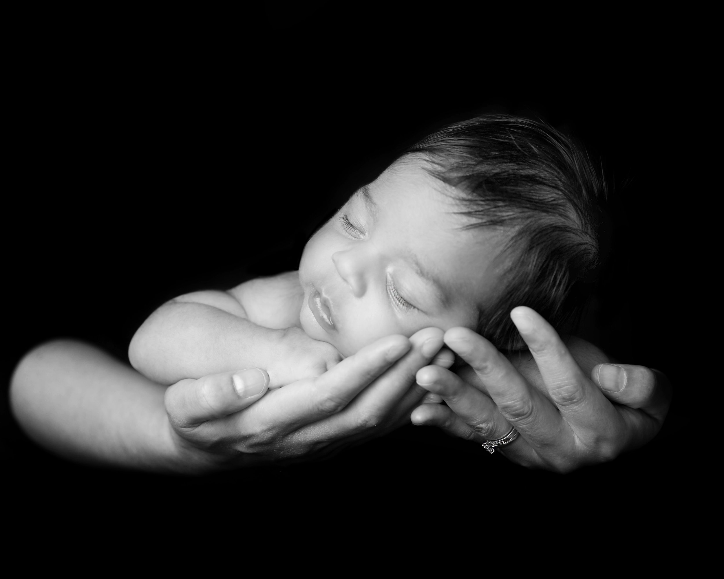 Black and white photo of a newborn in parents hands – artistic baby portrait photography