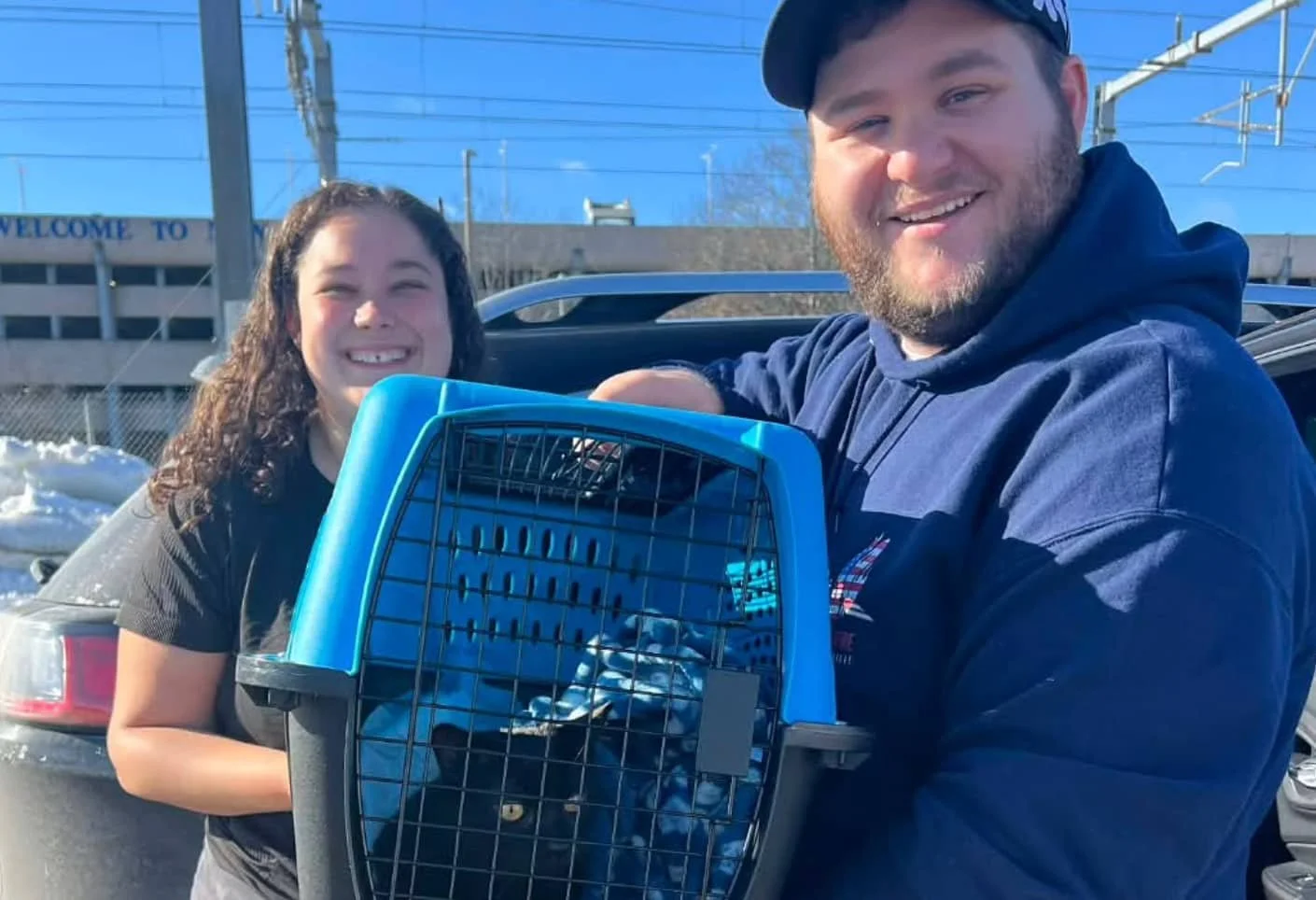 A young man and women with kind smiles hold up a kitty in a carrier as they safely transport her.