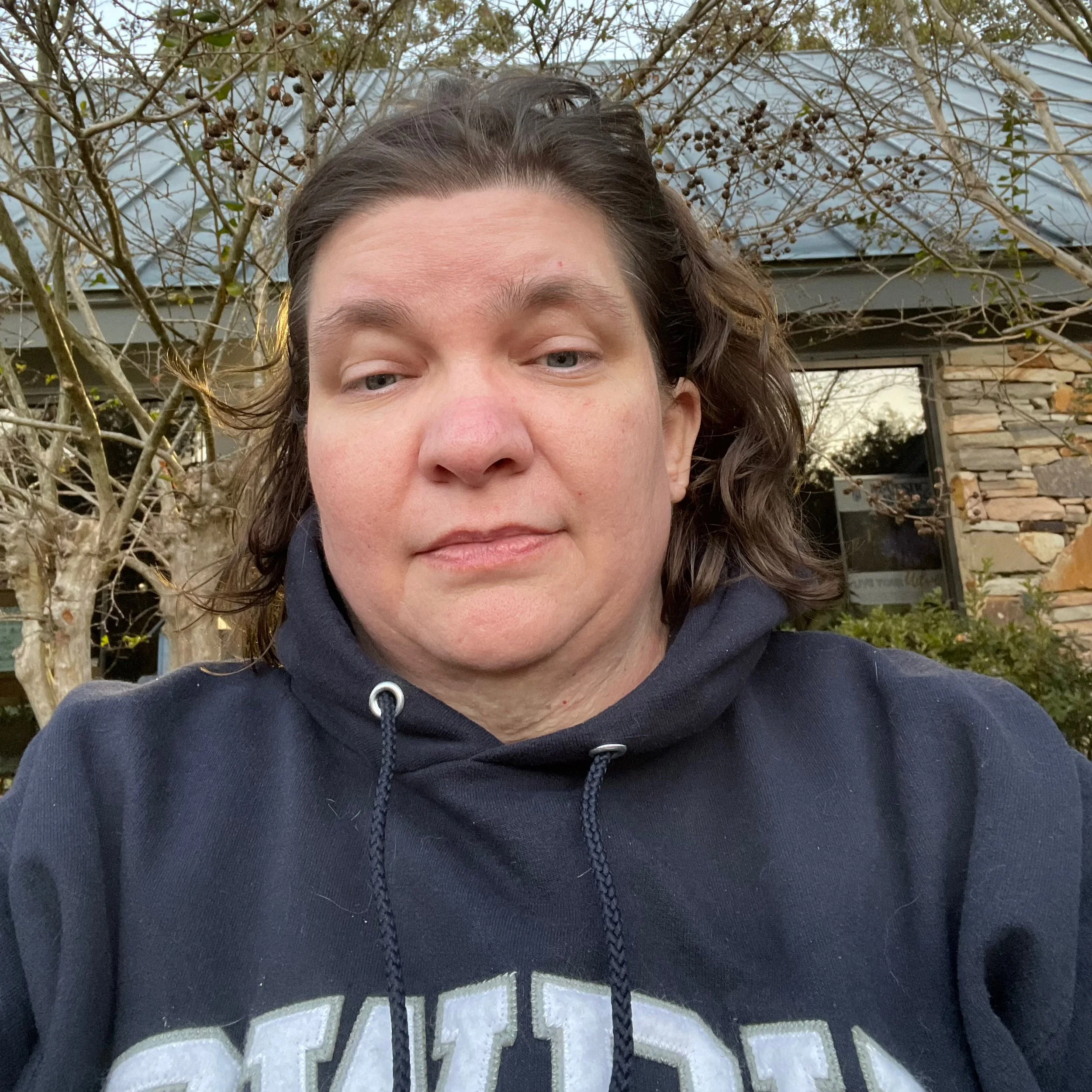 White woman in blue sweatshirt standing in front of a fall tree.