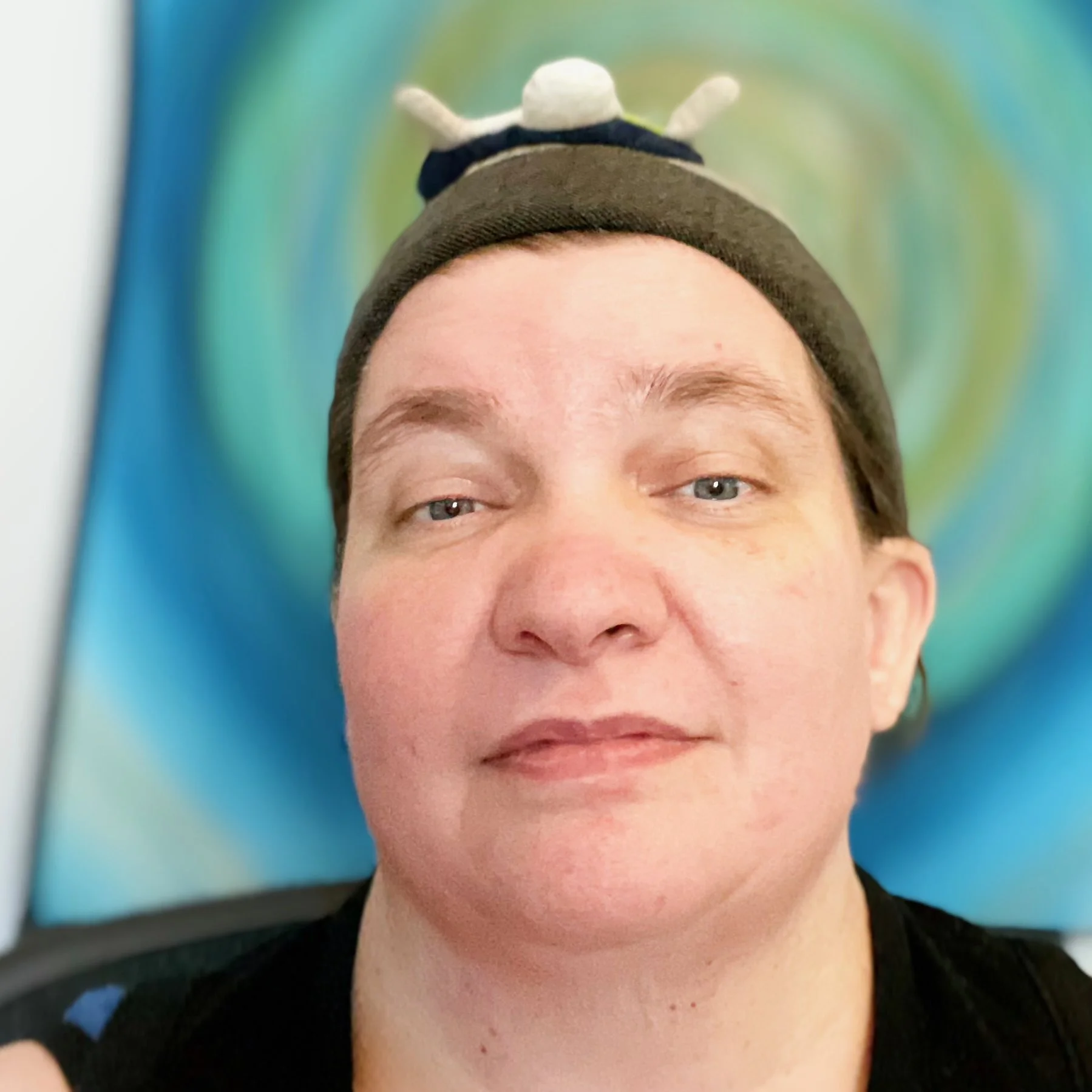 White woman wearing a brimless hat with a turtle coaster on her head.