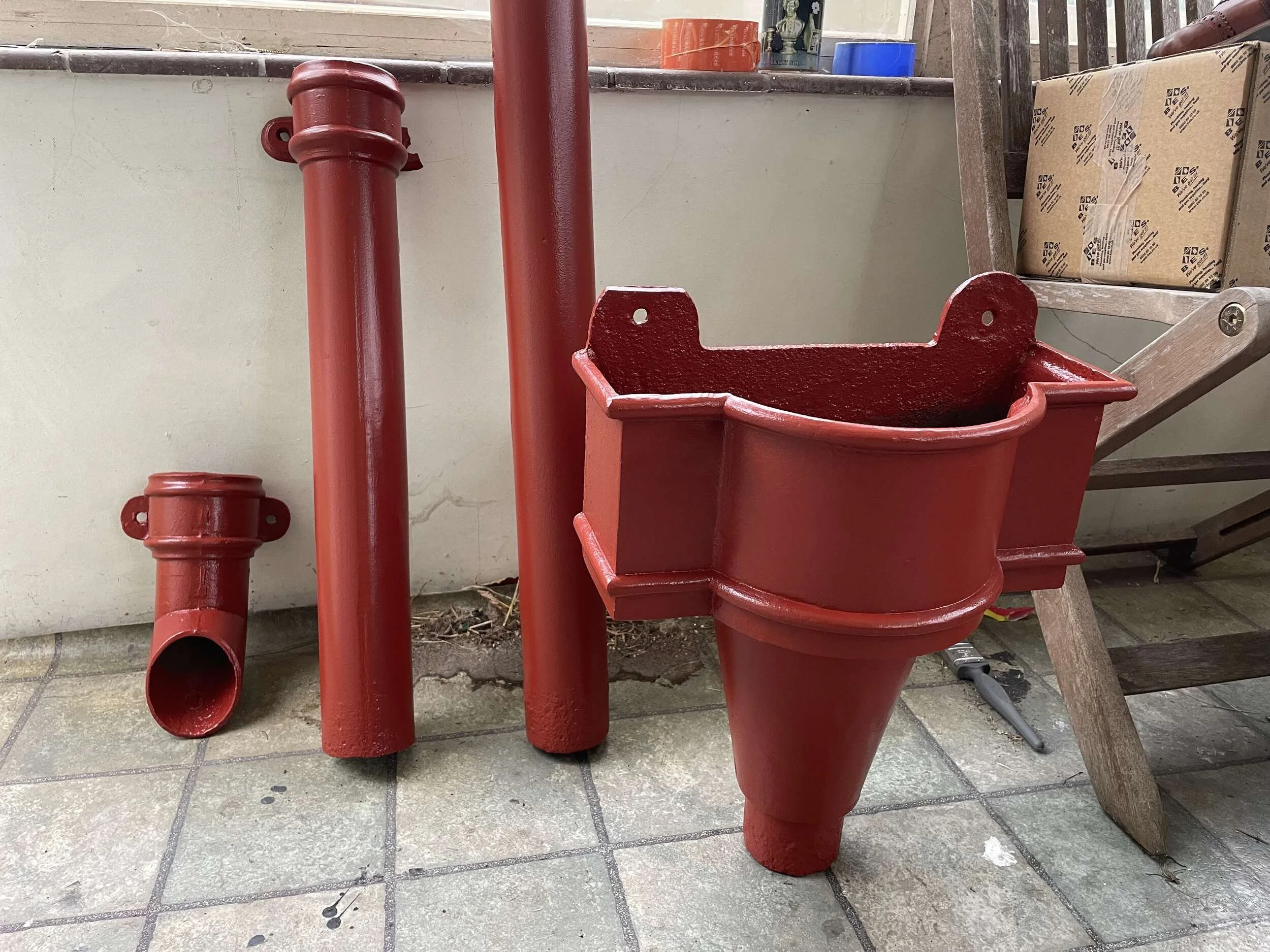Red-painted fire hydrant parts stored on a tiled floor, with some pipes and a window in the background.