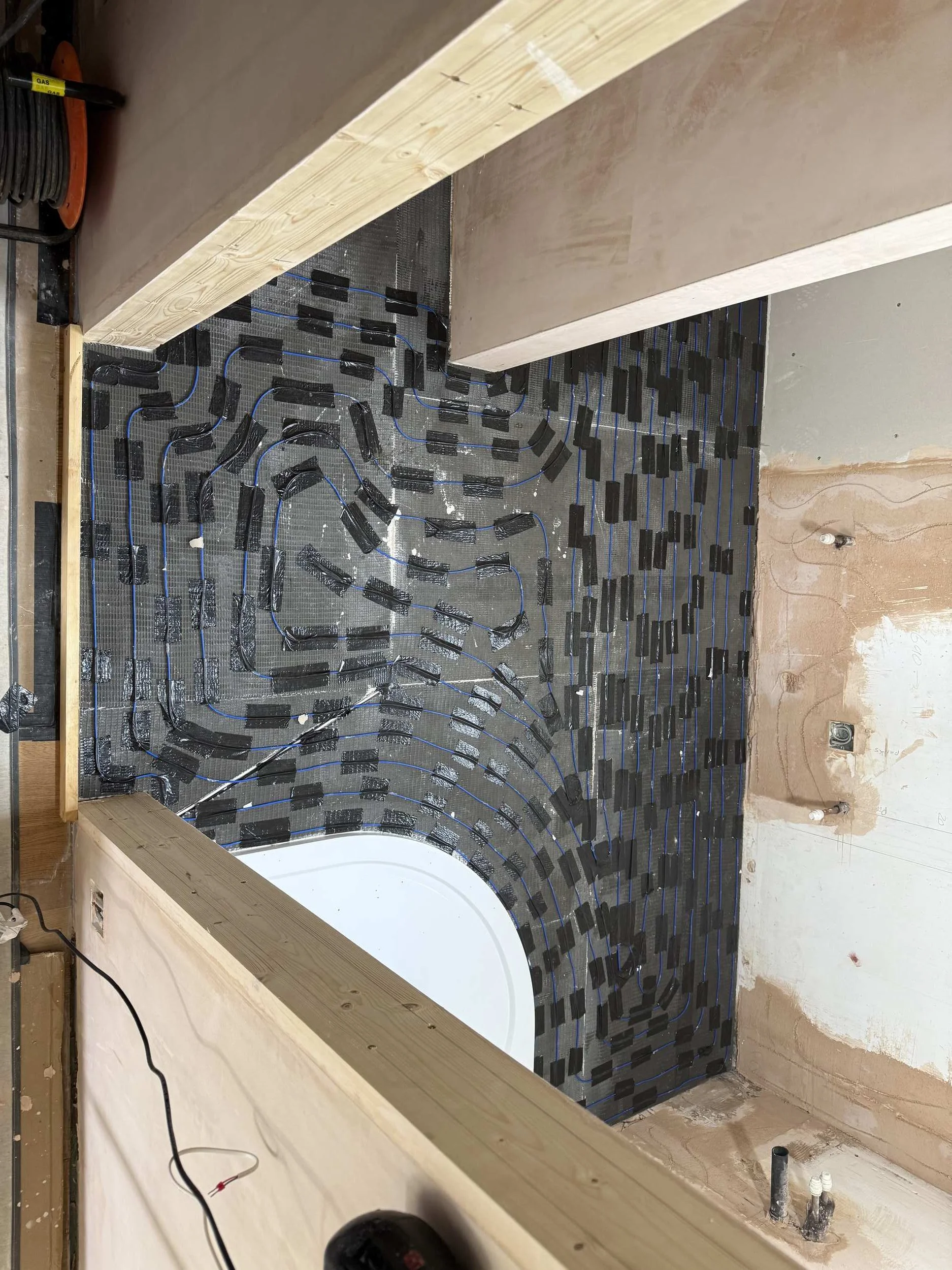 Bathroom undergoing renovation with heating cables and mesh laid out on the floor, side walls, and partially finished wall behind the bathtub.