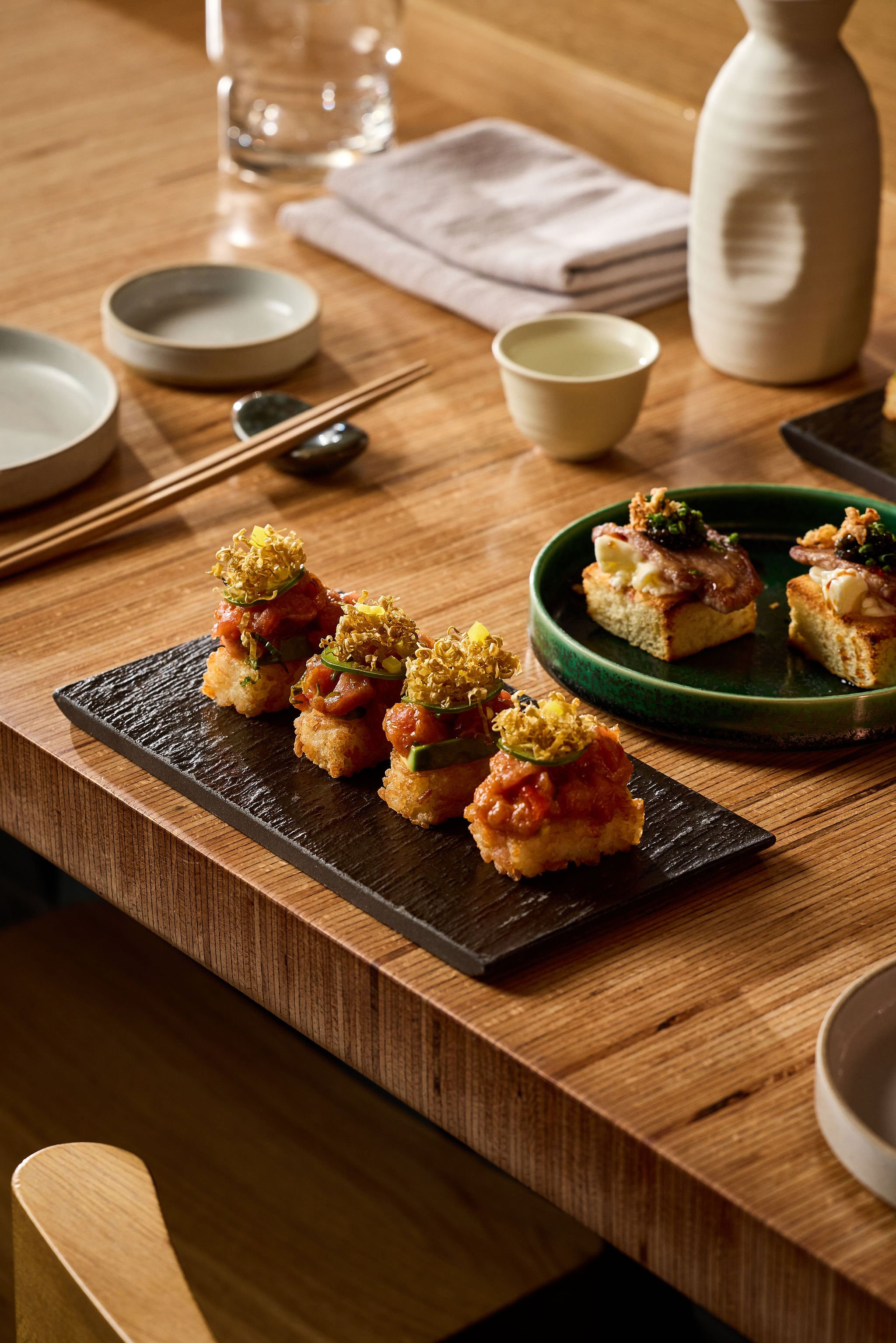 Japanese-style lunch or dinner setup with sushi, chopsticks, bowls, and a water glass on a wooden table.