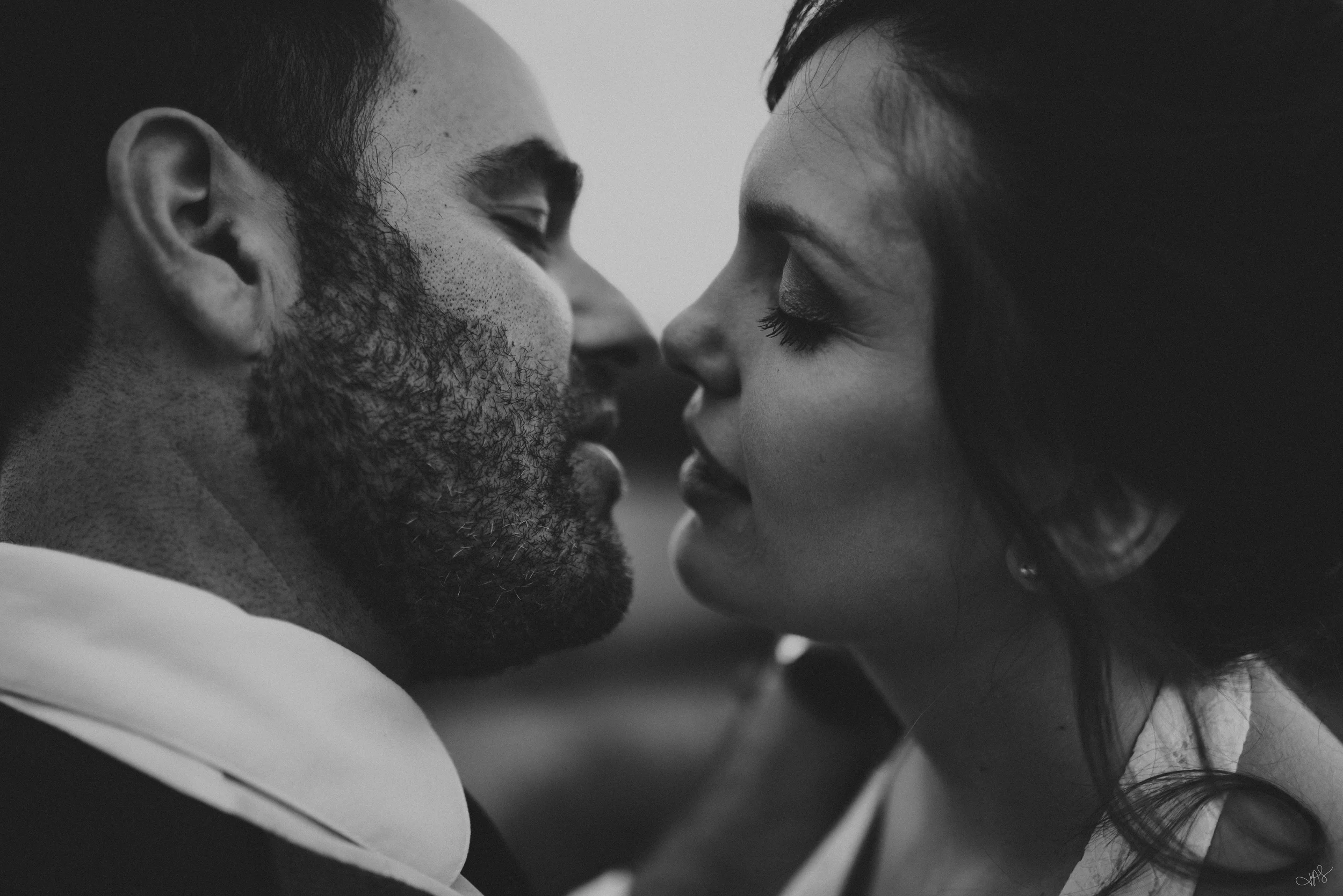 A black and white close-up photograph of a man and woman touching faces with their eyes closed, appearing intimate.