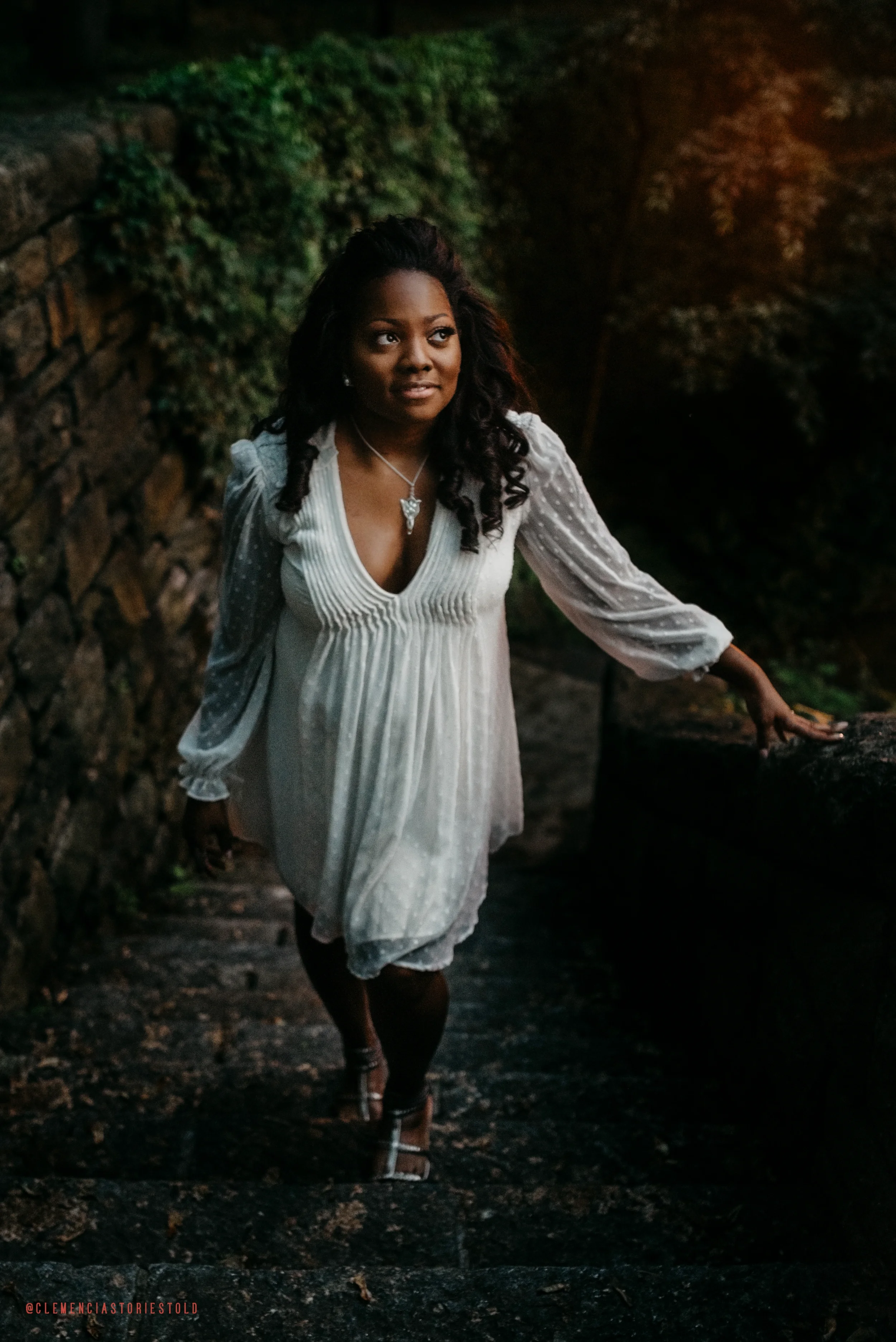A woman in a white dress walking up a stone staircase outdoors surrounded by greenery.