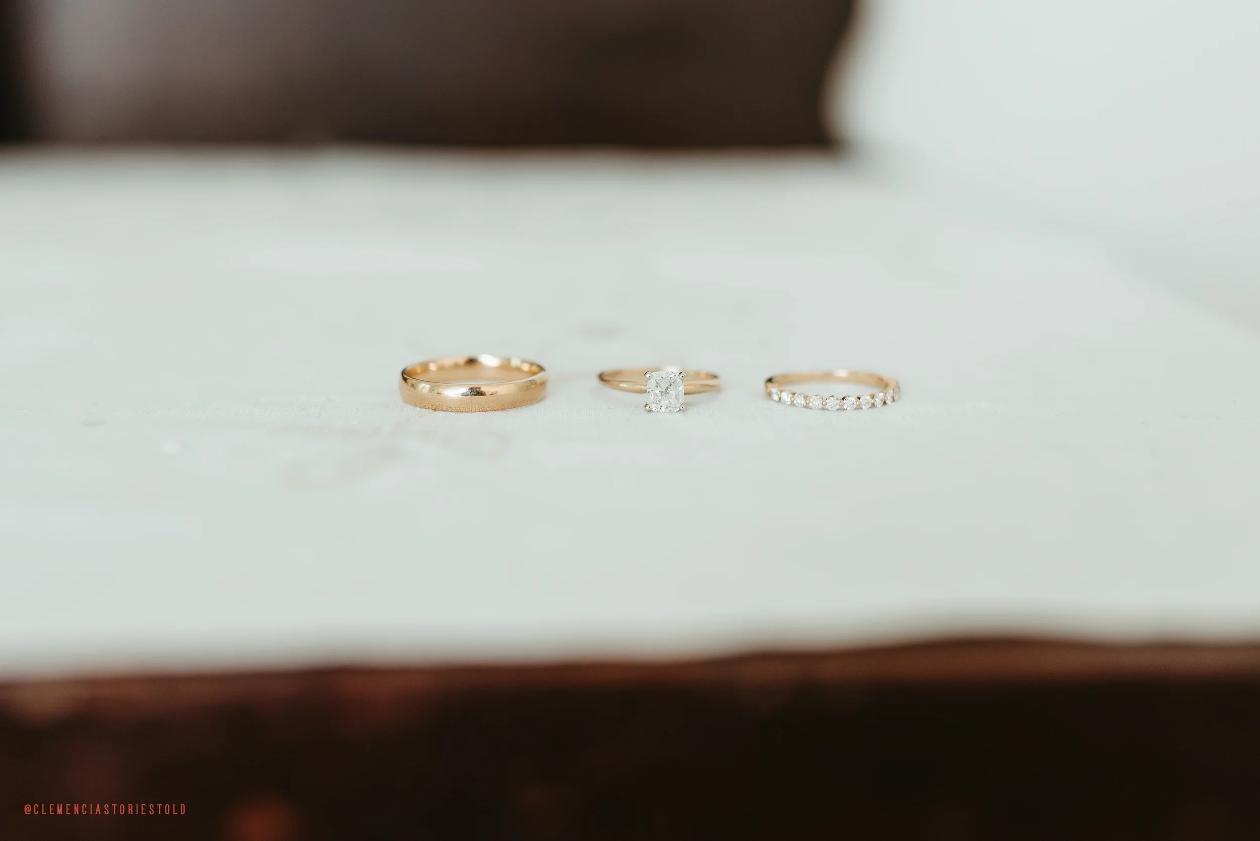Three gold rings, one plain band, one with a square diamond, and one with small diamonds, on a white surface.