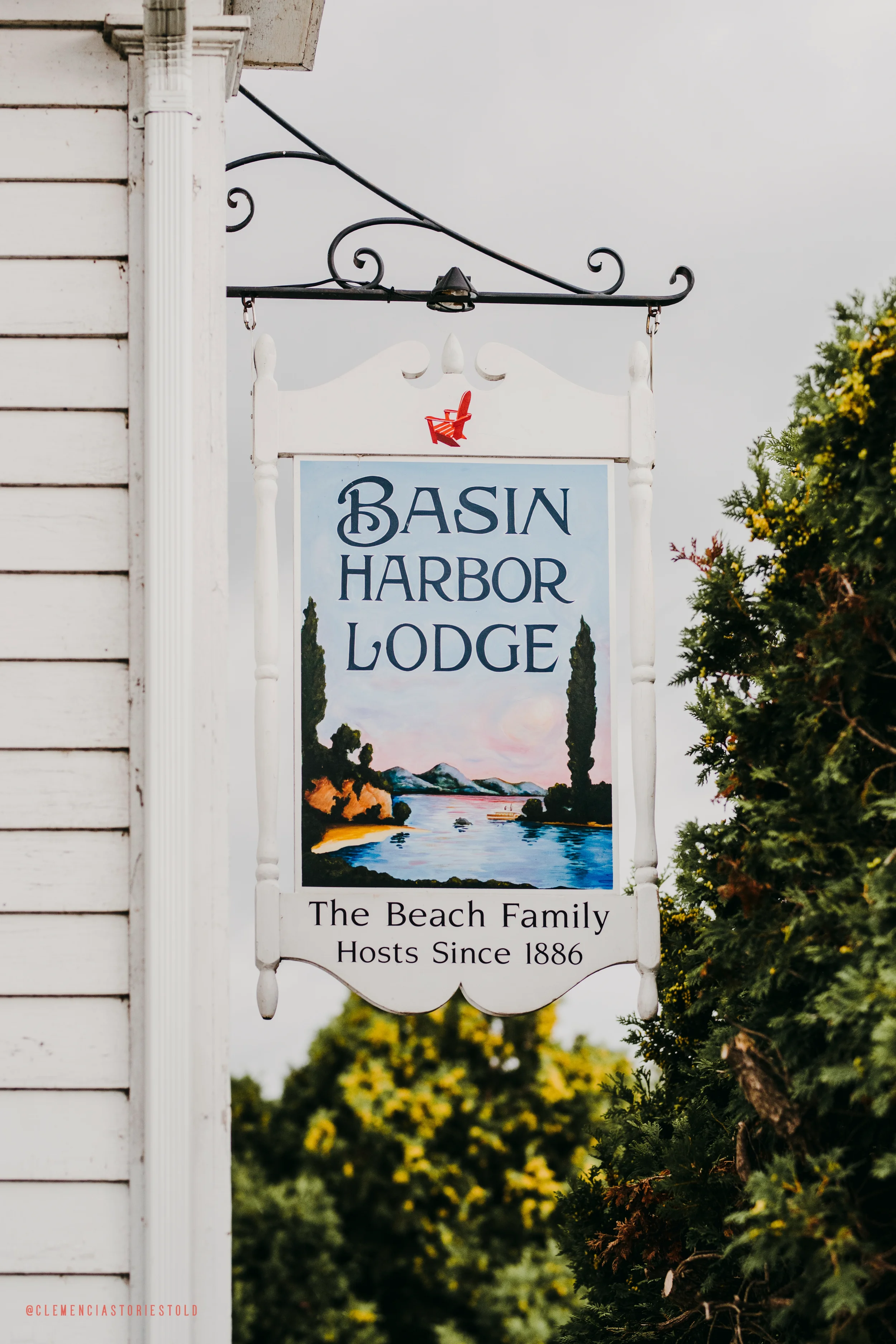 A hanging sign for Basin Harbor Lodge featuring an illustration of a river with trees and mountains in the background, with the text 'The Beach Family Hosts Since 1886' at the bottom.