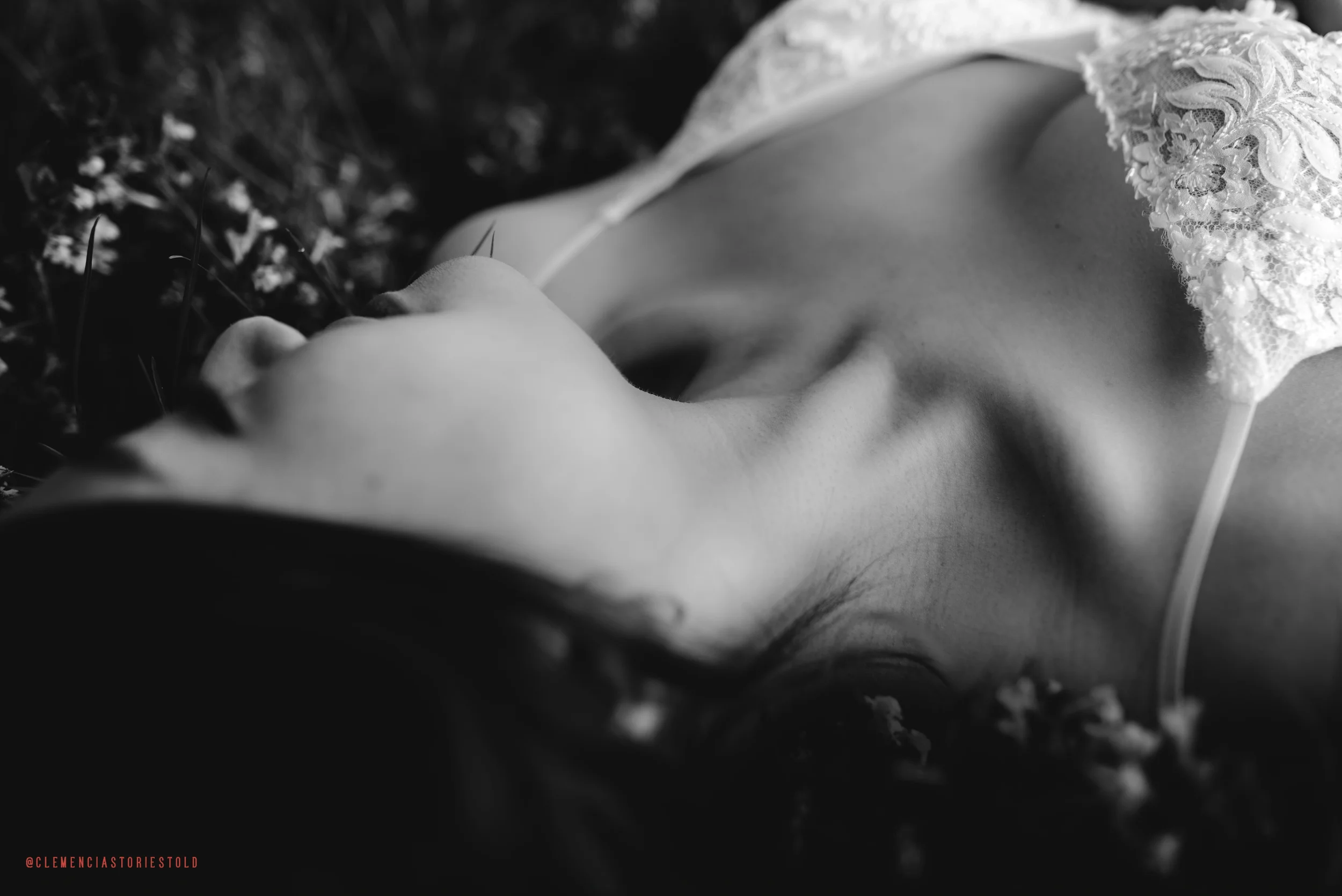 A black and white close-up of a woman's face and shoulder lying among flowers, dressed in lace clothing.