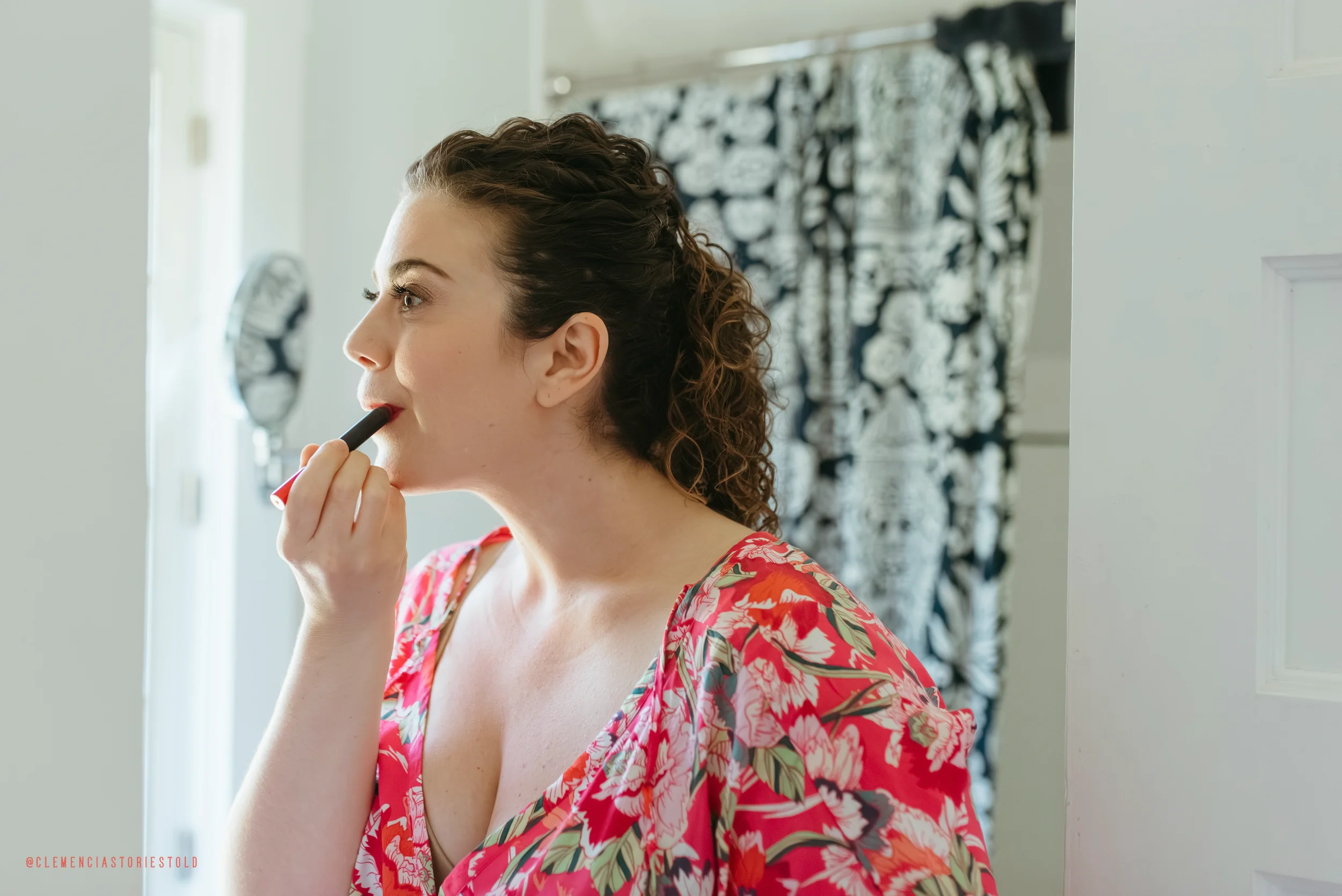 Woman with curly hair applying lipstick in front of mirror