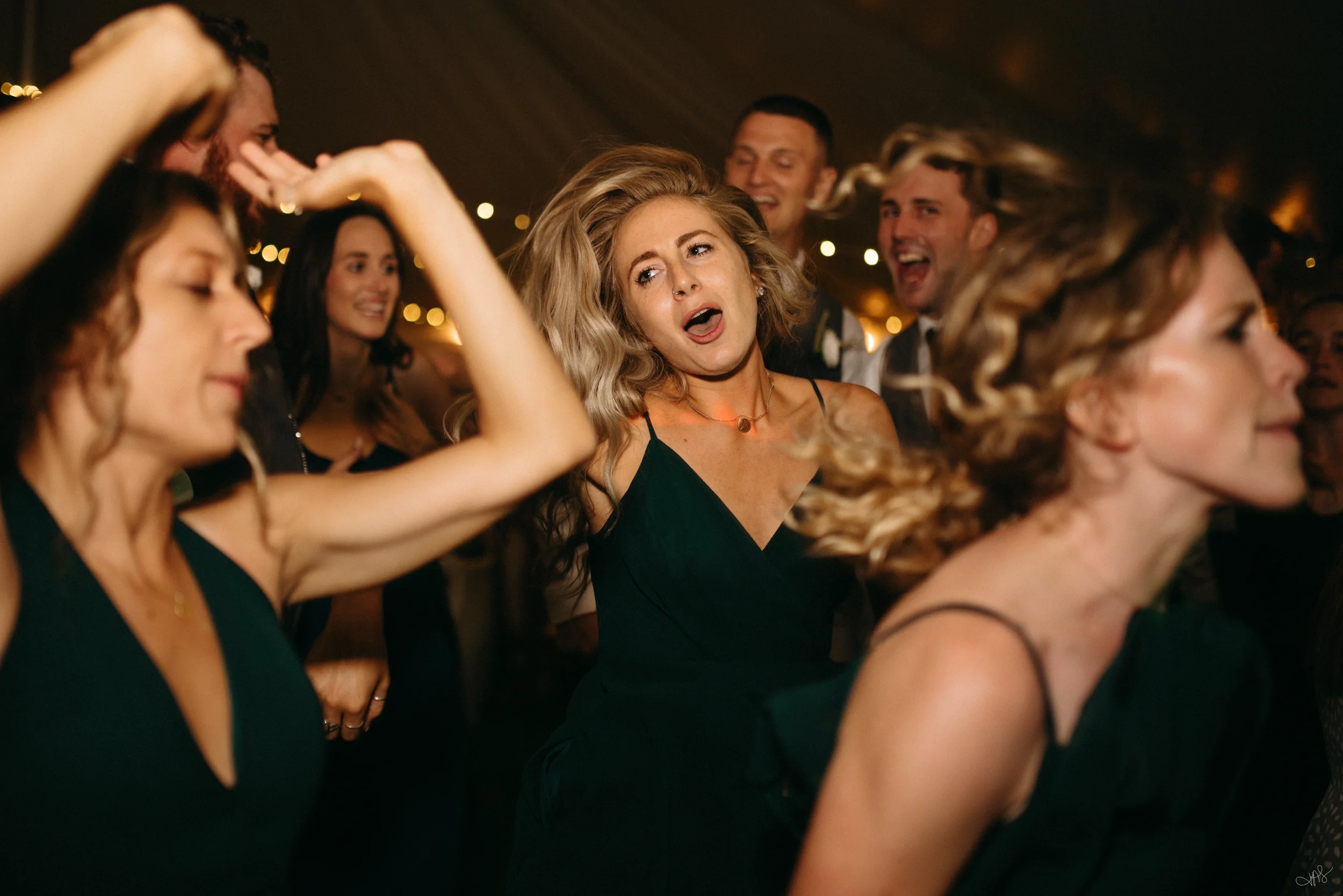 Group of people dancing and enjoying a celebration at night with string lights in the background.