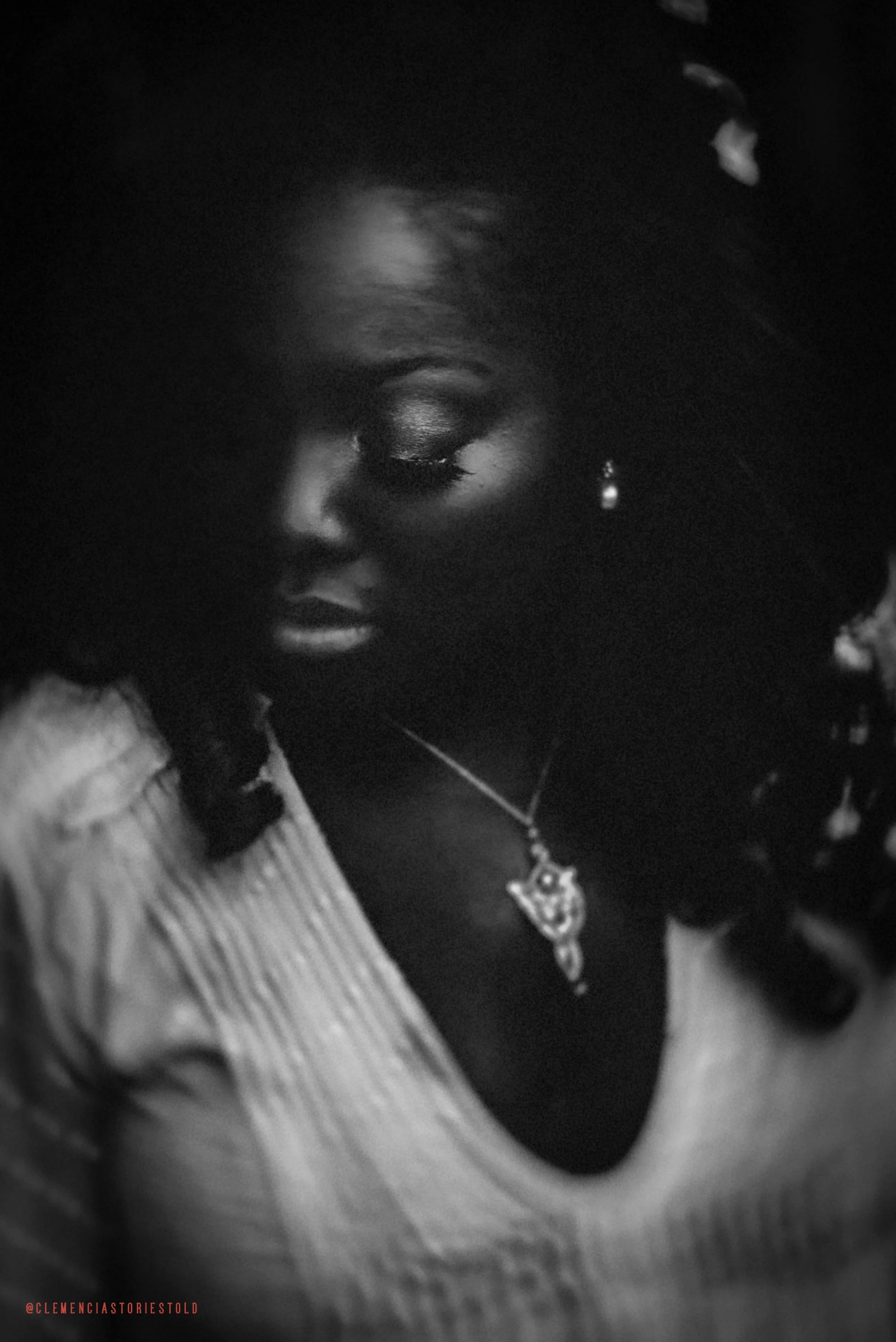 Black and white photo of a woman with closed eyes, wearing a necklace and earrings, with soft lighting highlighting her face.