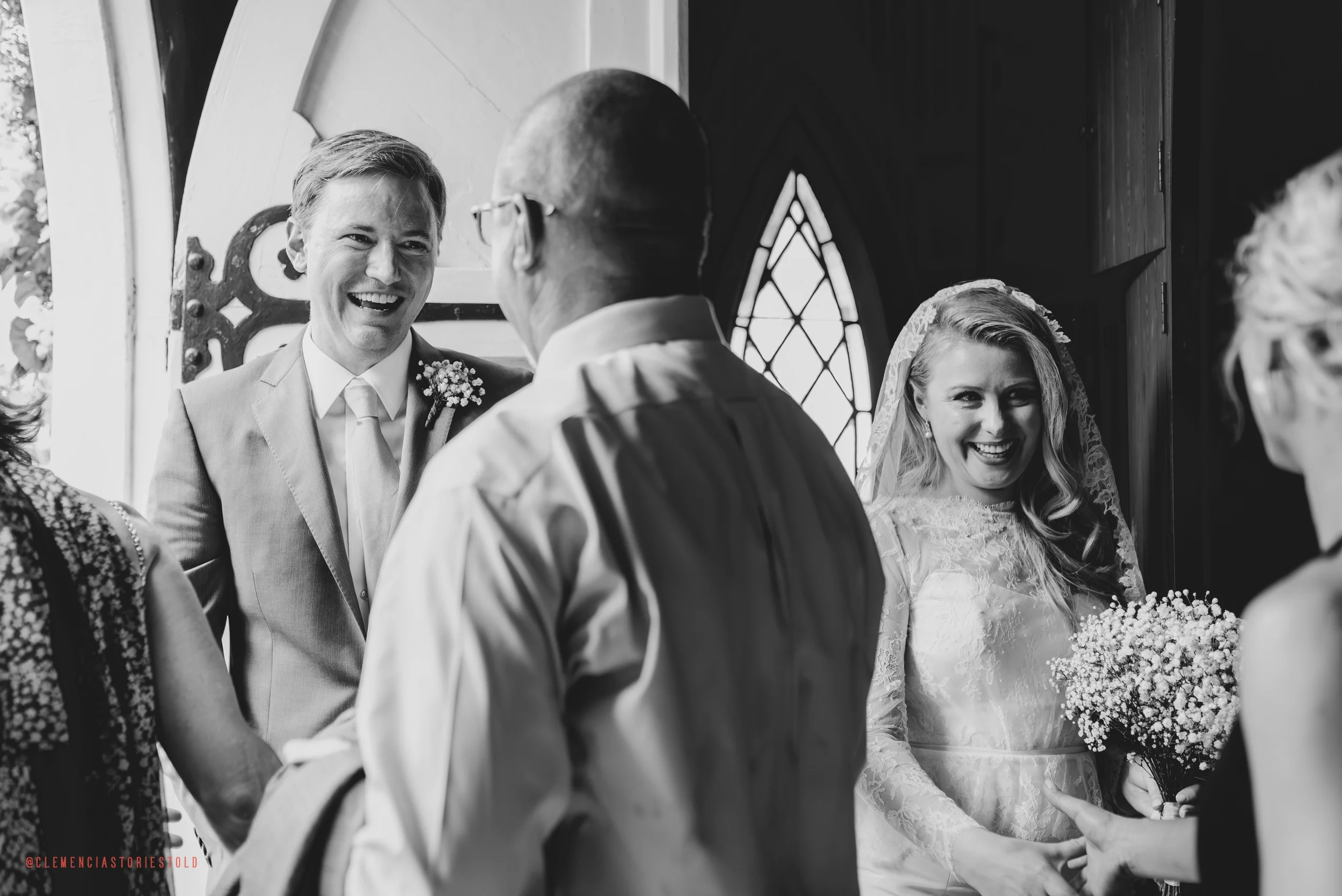 Black and white photo of a wedding ceremony inside a church, featuring the bride and groom smiling and interacting with guests.