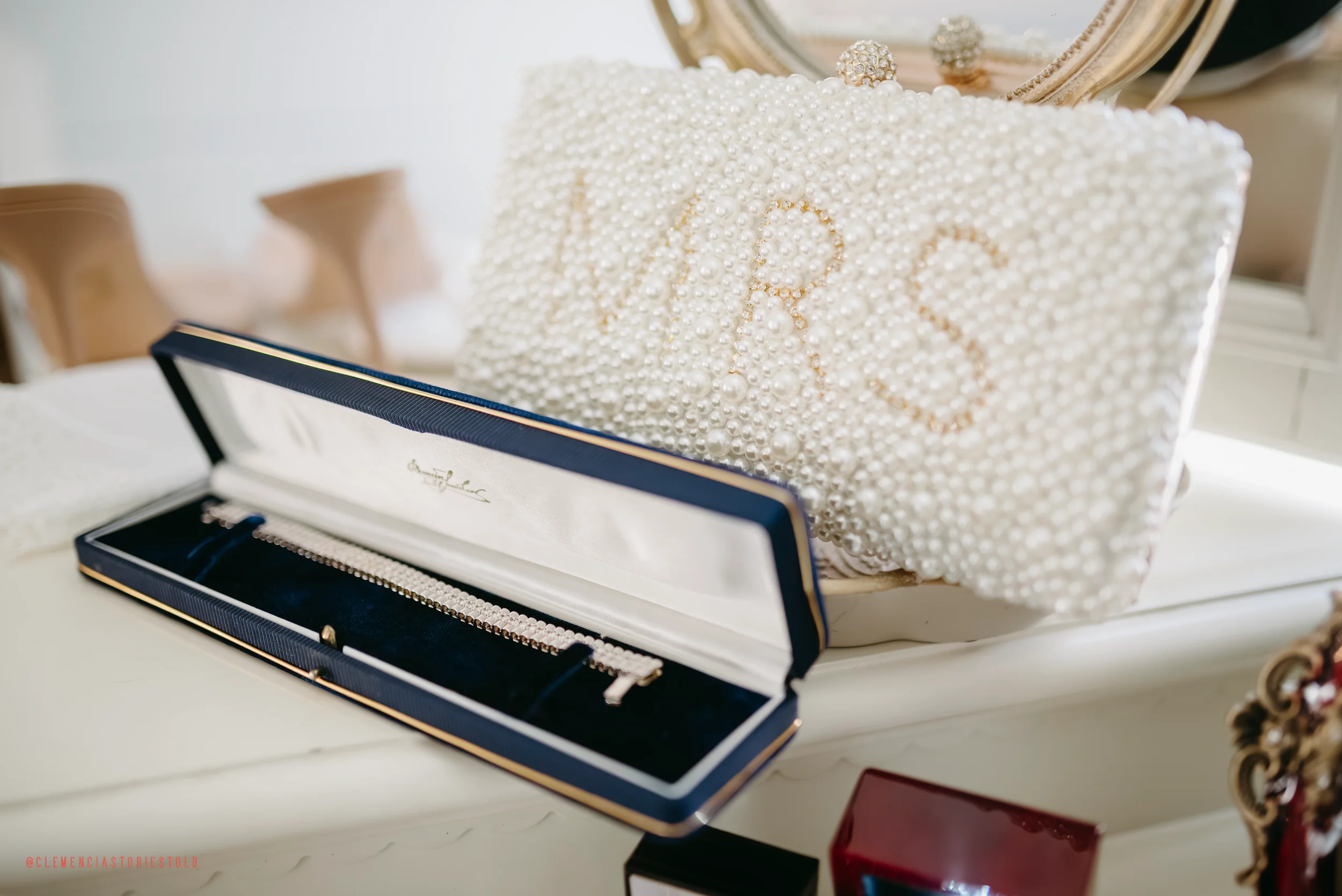 Pearl-embellished pillow with the word 'Love' spelled out in gold beads, and an open jewelry box containing a pearl bracelet, placed on a white dresser with other decorative items.