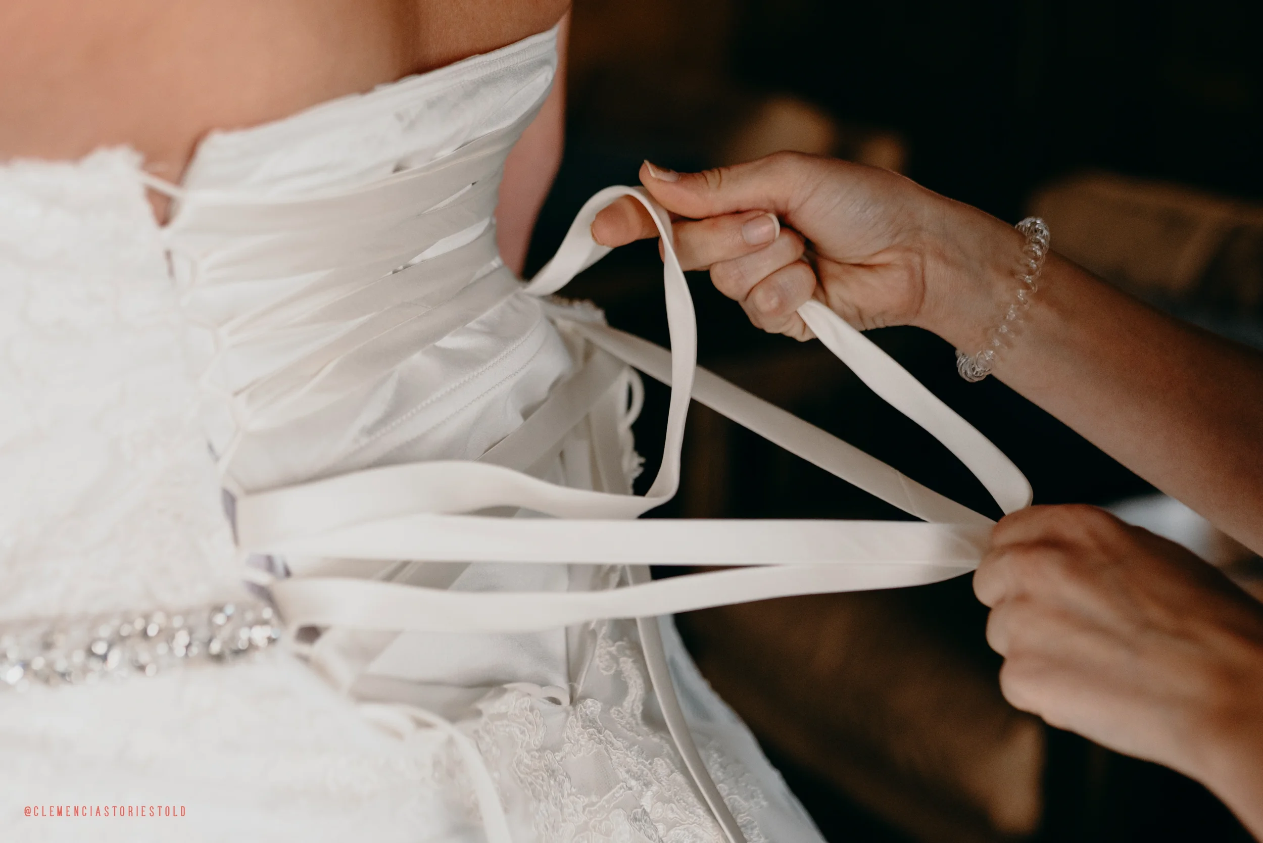 Person's hands tying the back laces of a white wedding dress.
