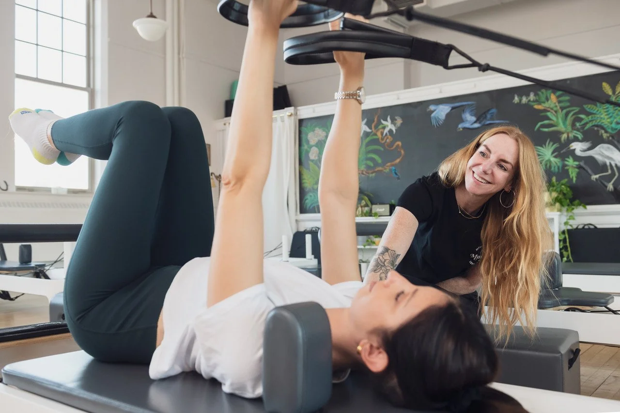 Two people practicing Pilates with a reformer at Muse Movement