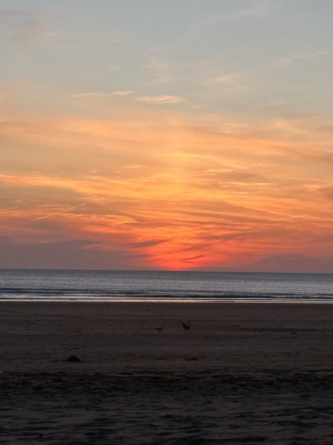 Sunset over the ocean with a colorful sky and a sandy beach in the foreground.