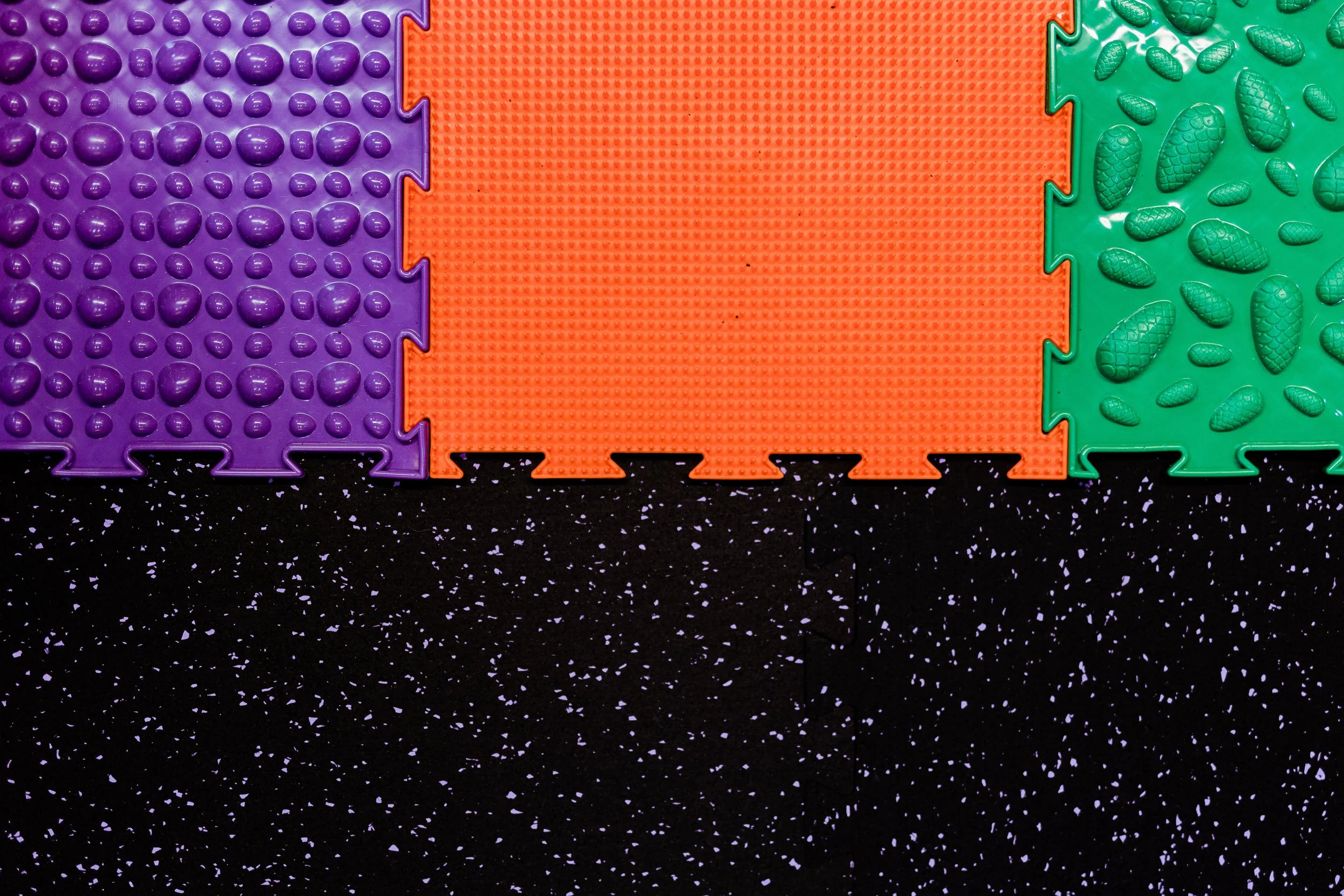 Colorful interlocking foam tiles in purple, orange, and green on a speckled black and white floor.