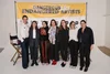 Group of seven women standing in front of a yellow and white backdrop with text that reads "DANGEROUS ART ENDANGERED ARTISTS" at an art event or exhibition.