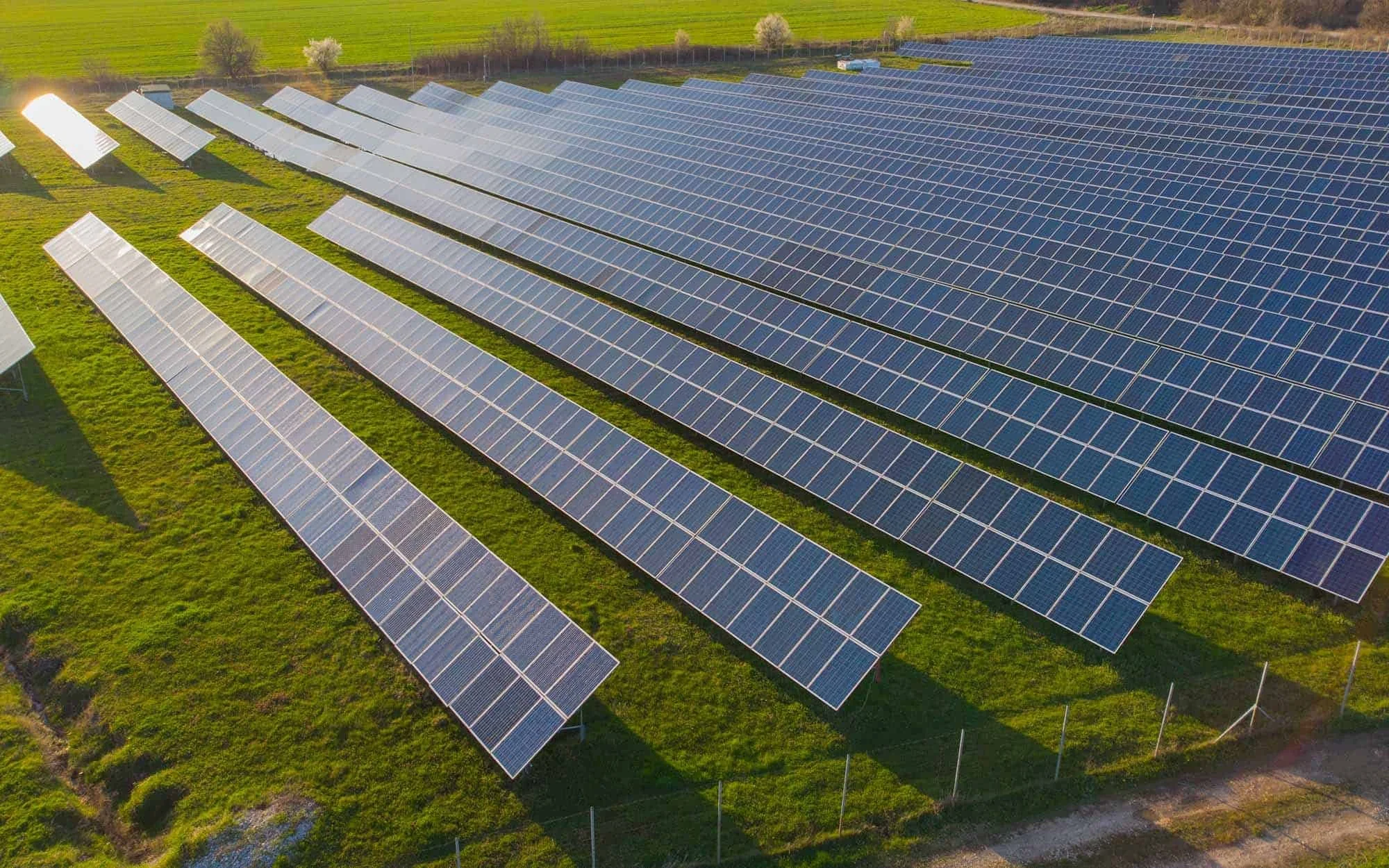Aerial view of a solar farm with multiple rows of solar panels installed on grassy land.