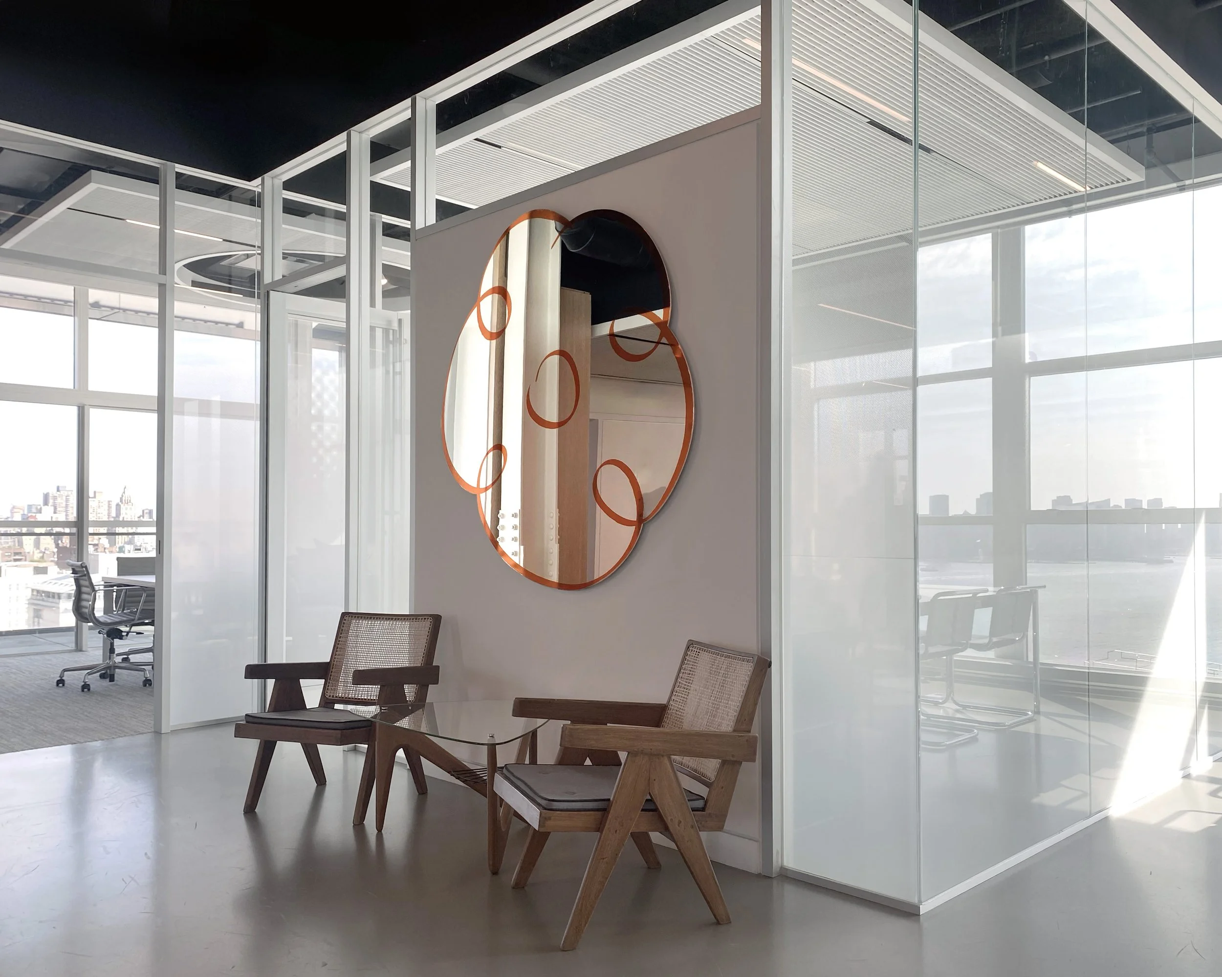 Modern conference room with glass walls, wooden chairs, and a round mirror with orange rings on the wall.