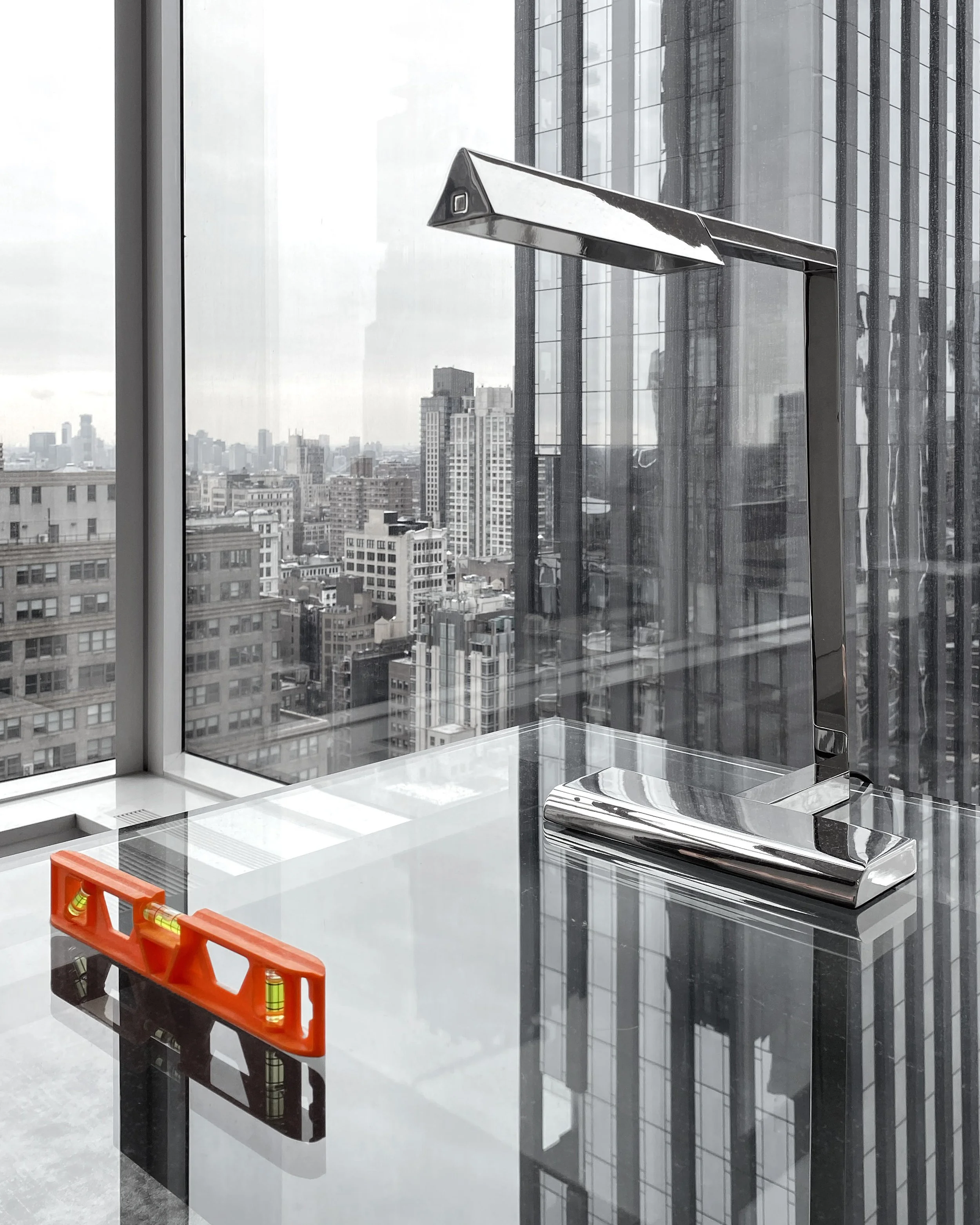 Interior of a modern office building with large windows showing a cityscape, featuring a metallic desktop lamp, a white counter with a red tool organizer, and safety level tools inside.