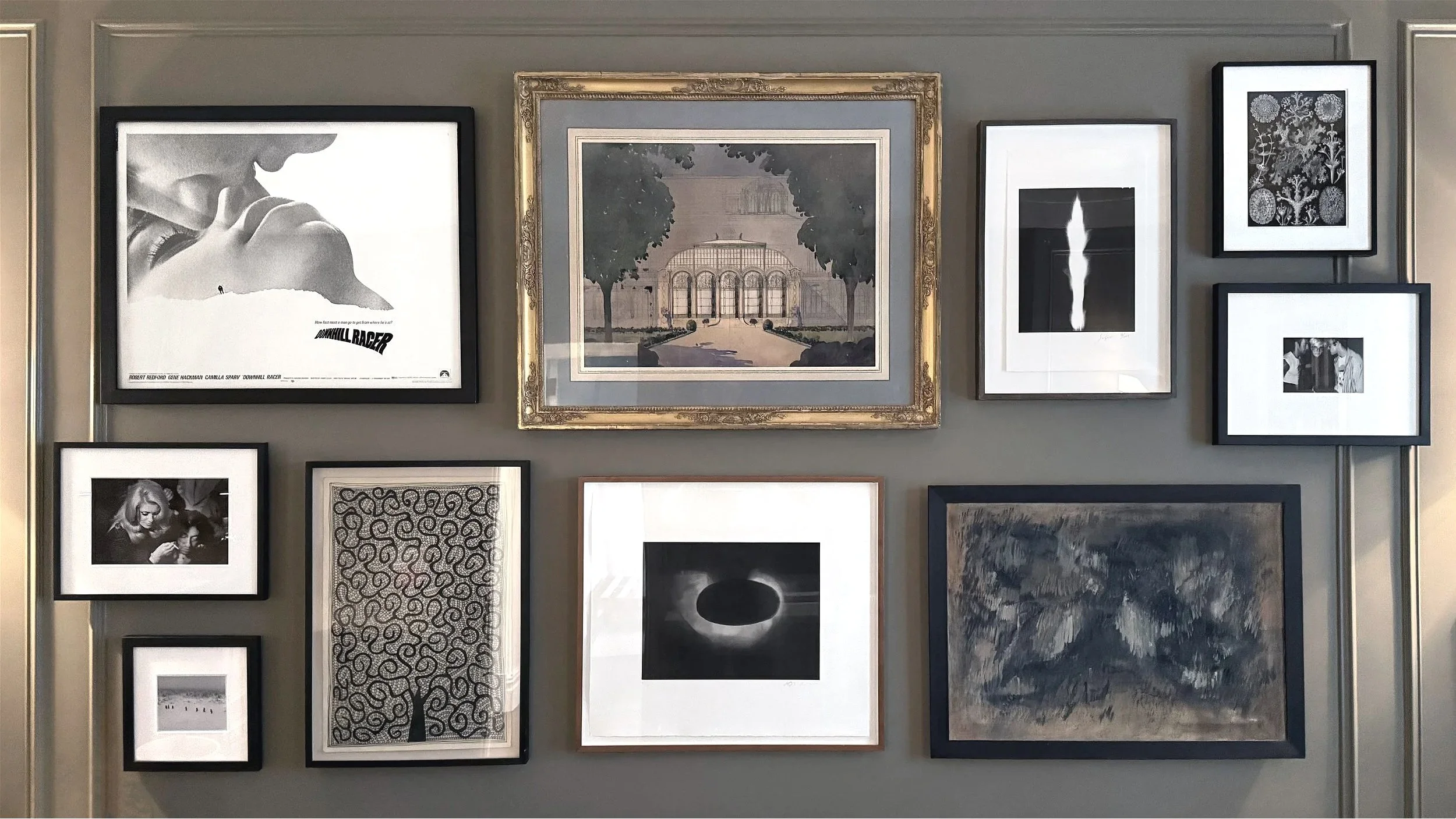 A gallery wall with various black-and-white framed artwork, including photographs, illustrations, and abstract designs, arranged on a gray wall.