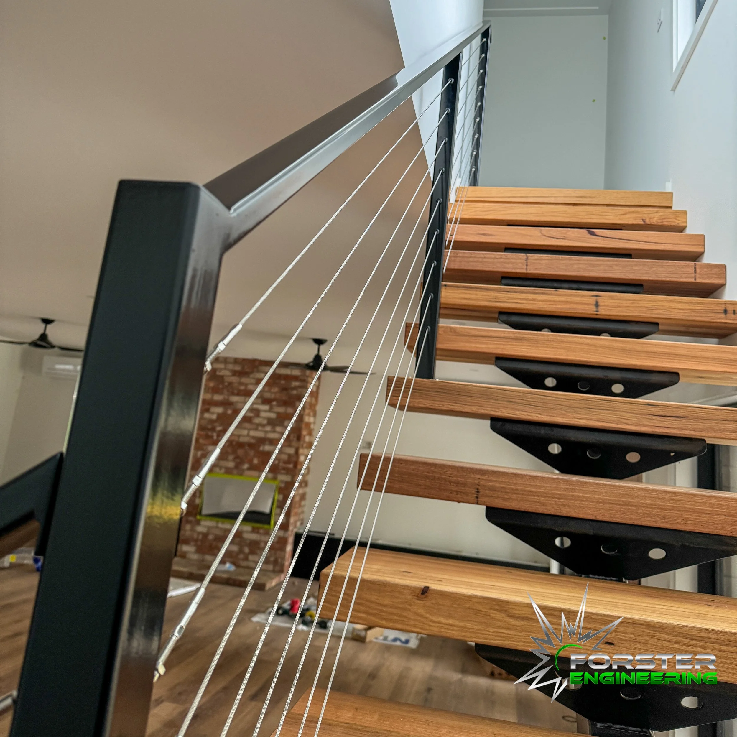 Close-up of a staircase with wooden steps and metal support brackets, viewed from below. Modern interior design with a cable railing system.