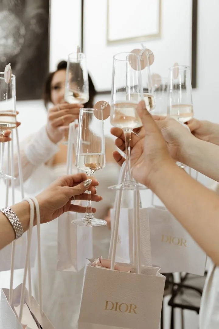 Group of hands holding champagne flutes and Dior gift bags, celebrating.