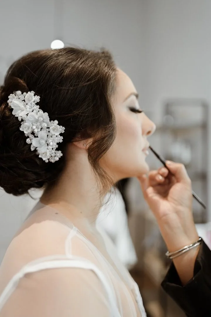 A woman getting her makeup applied, with floral hair accessory.