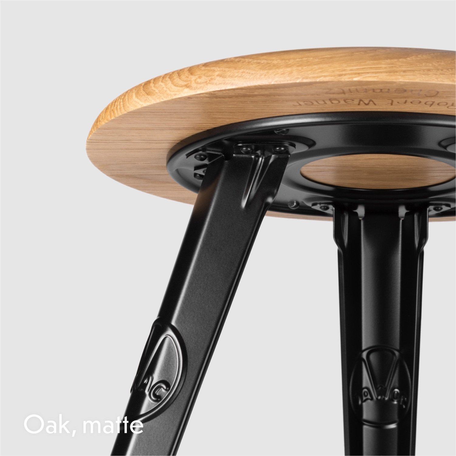 Rowac Model 1 industrial Schemel or workshop stool – detail view of riveted metal or steel leg and seat base. Oak seat top and frame in matte black.