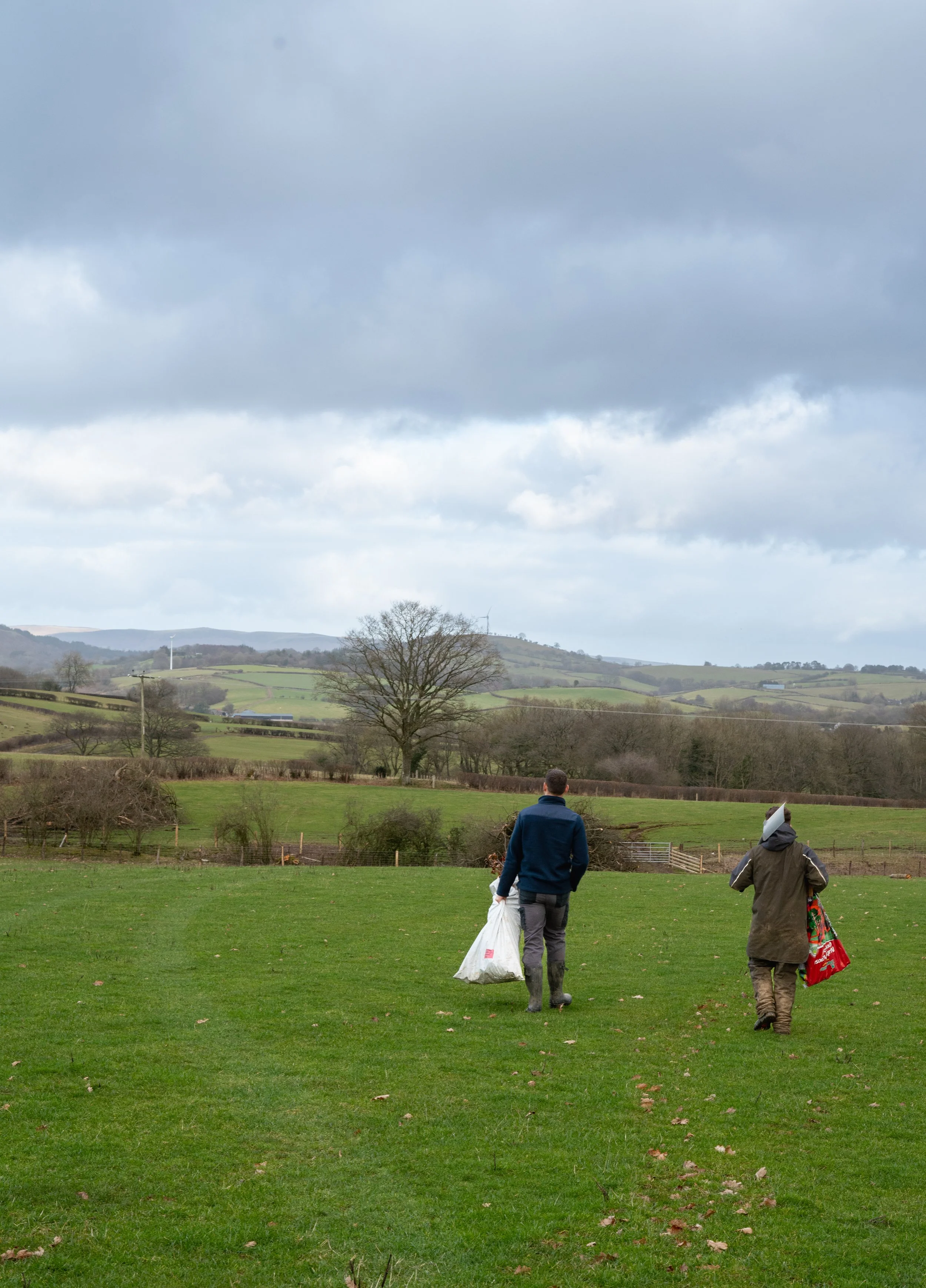 Two figures carrying tree planting equipment.