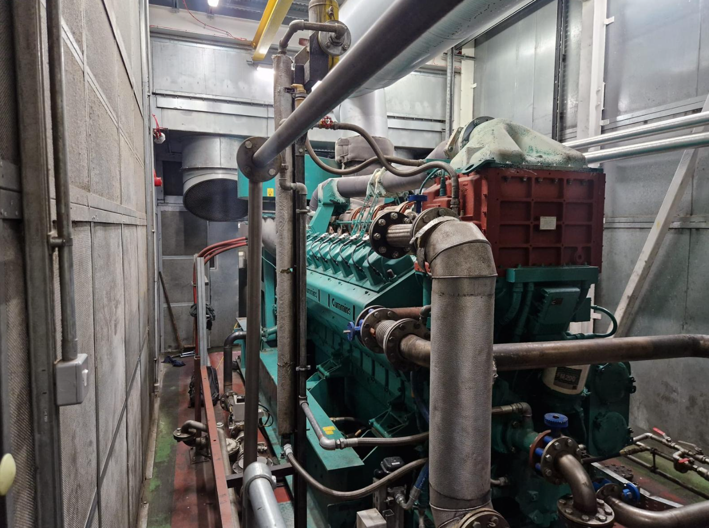 Industrial engine and piping system inside a metal-walled room.