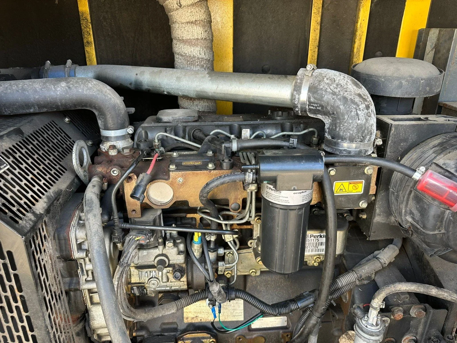 Close-up view of an industrial engine with various pipes, hoses, and metal components, some showing signs of dirt and wear.