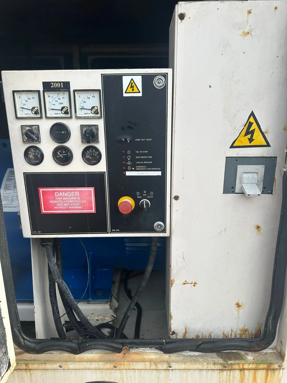 Electrical control panel with gauges, warning signs, and switch, mounted on a white metal box with rust spots.