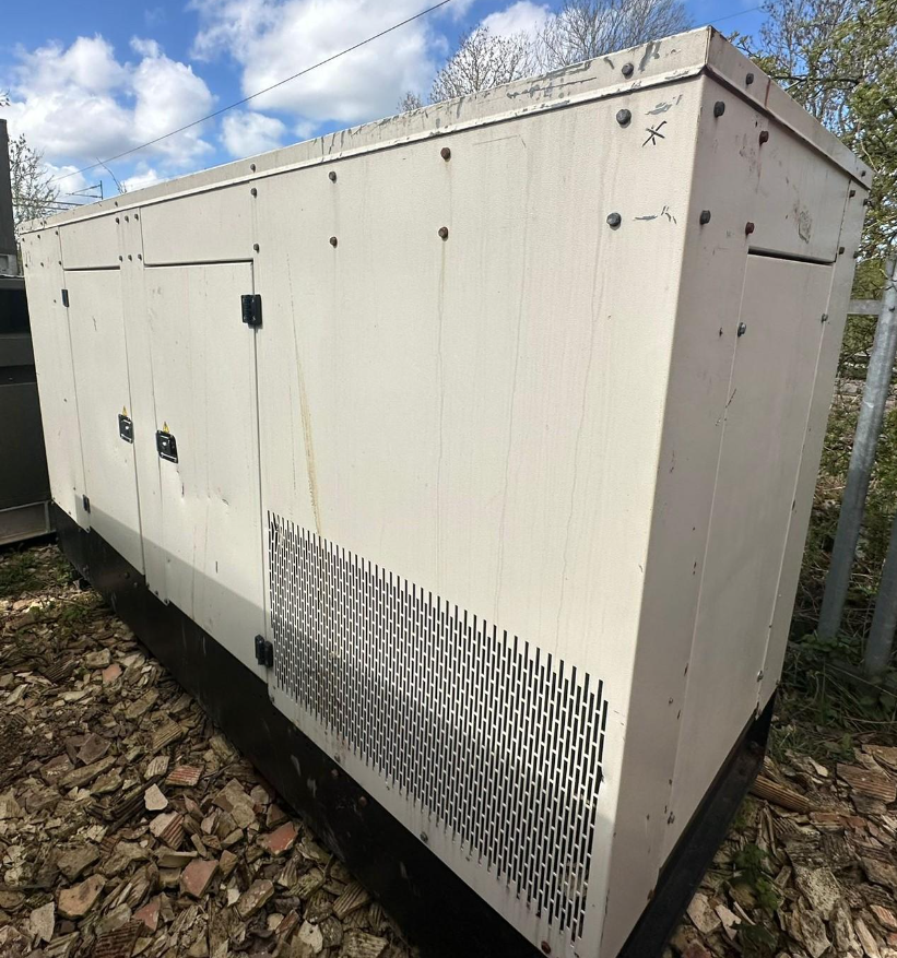 A large, beige industrial generator located on a bed of rocks outdoors, with a brown and black base, metal vents, and a couple of black handles on the front.