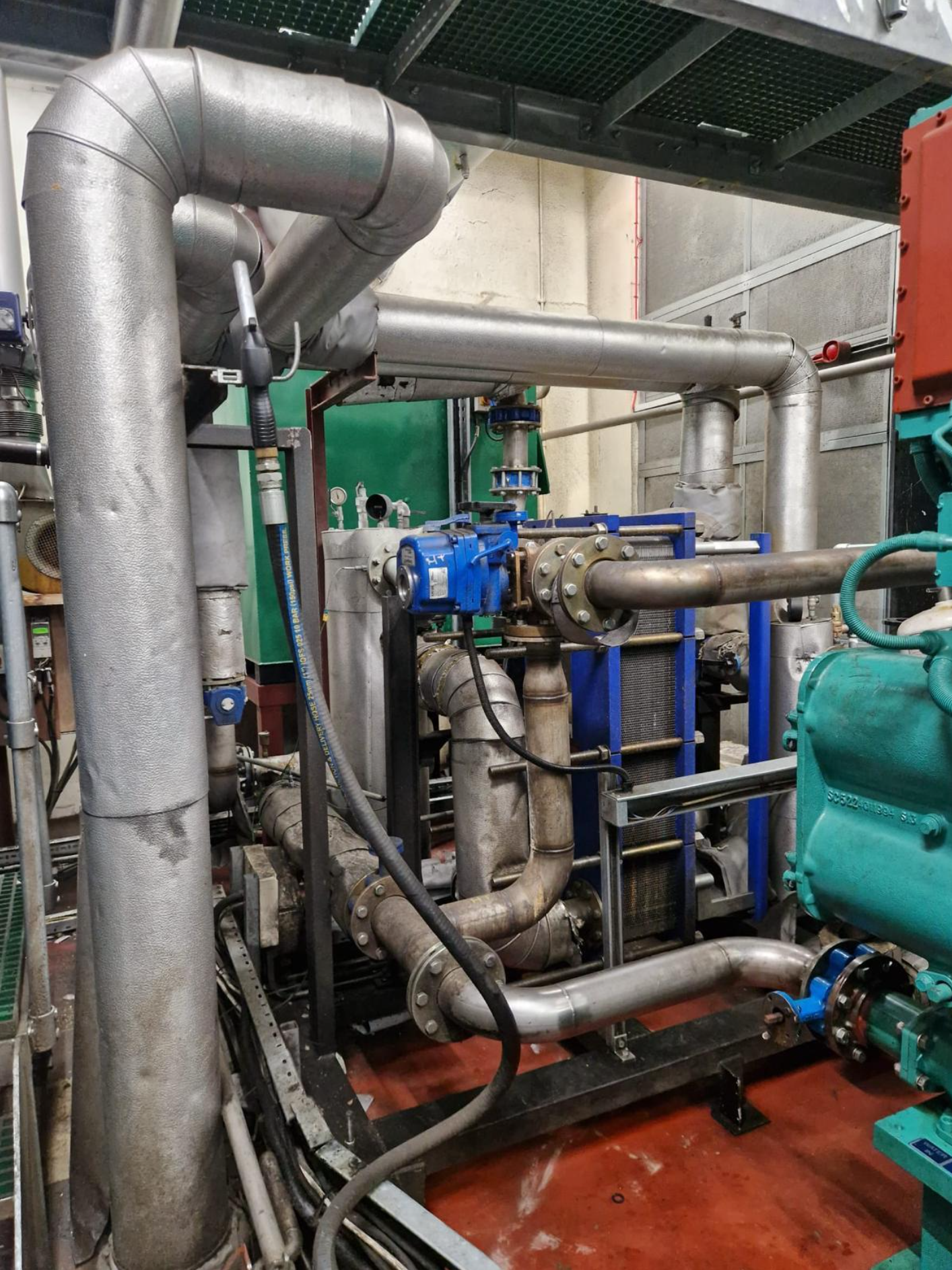 Industrial mechanical room with large metallic pipes, valves, and machinery.