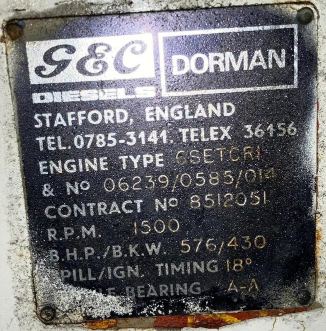 Metal identification plate for a diesel engine, showing contact information, engine type, serial number, contract number, RPM, power specifications, ignition timing, and bearing details, mounted on a machine or vehicle.