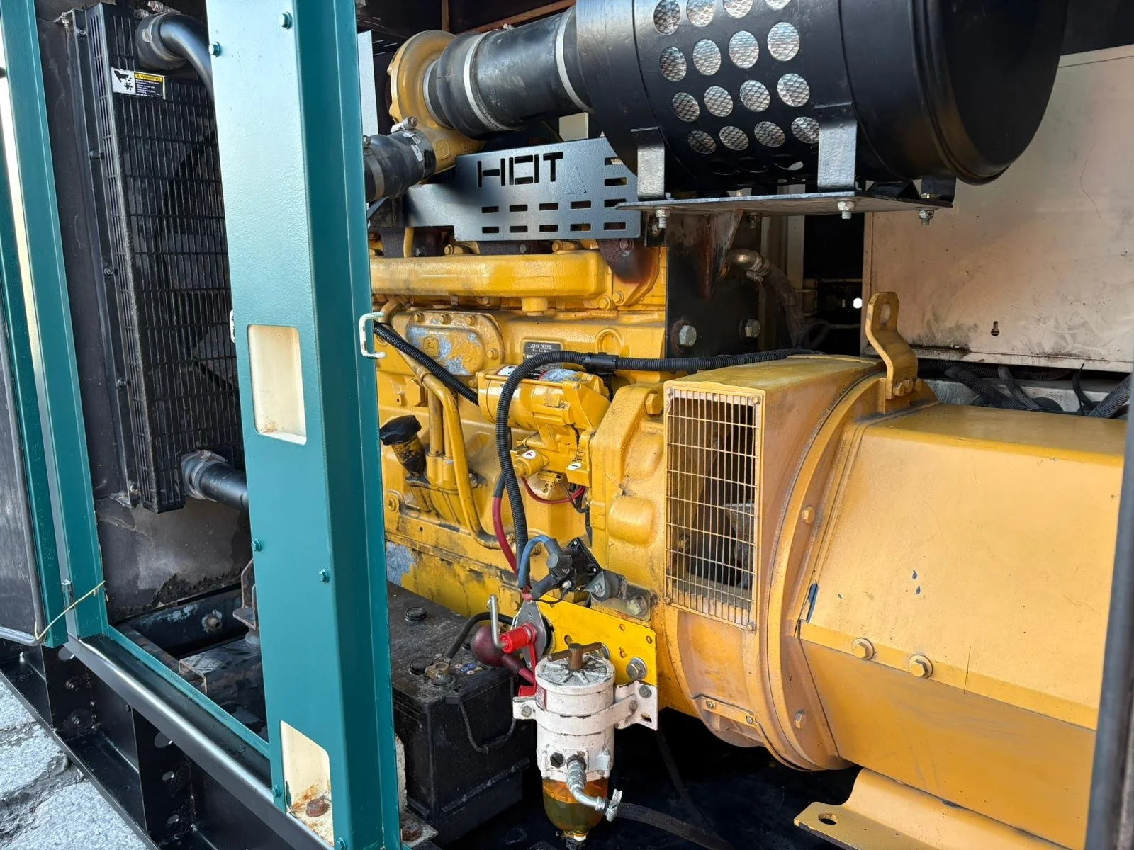 Close-up of a yellow industrial generator engine with black and teal components, hoses, and filters.