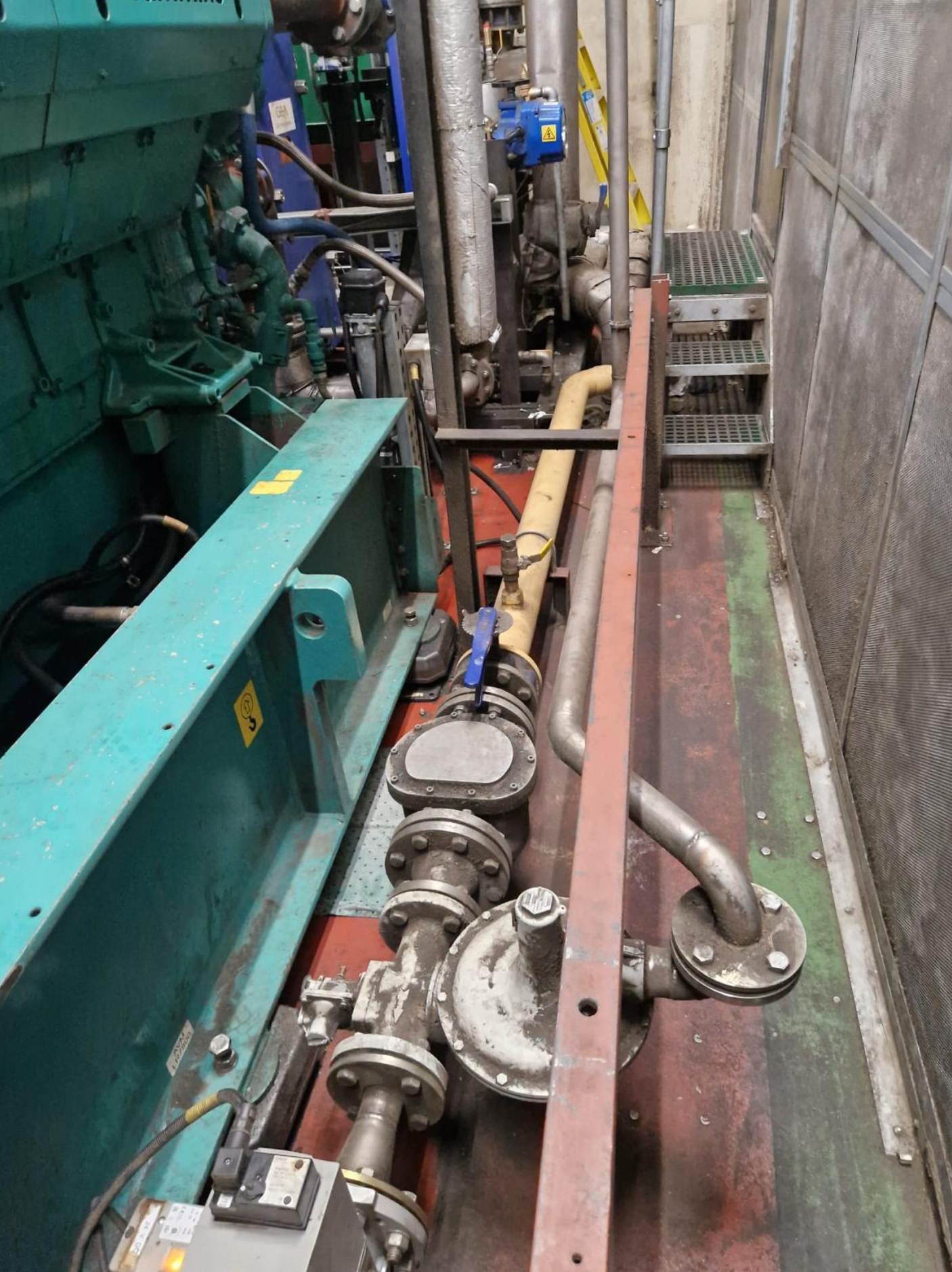 Industrial machinery with pipes, valves, and control units installed on the floor of a factory or mechanical room.