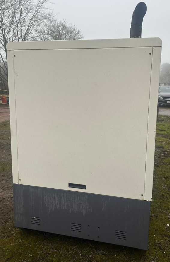 Large outdoor white and black electrical or utility unit on grassy area, with trees and cars in the background.