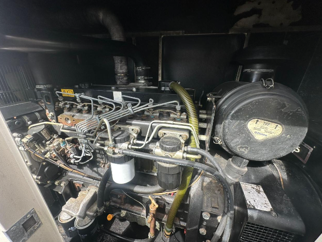 Close-up of a black industrial engine with various pipes, wires, and components, including a large black circular part on the right side