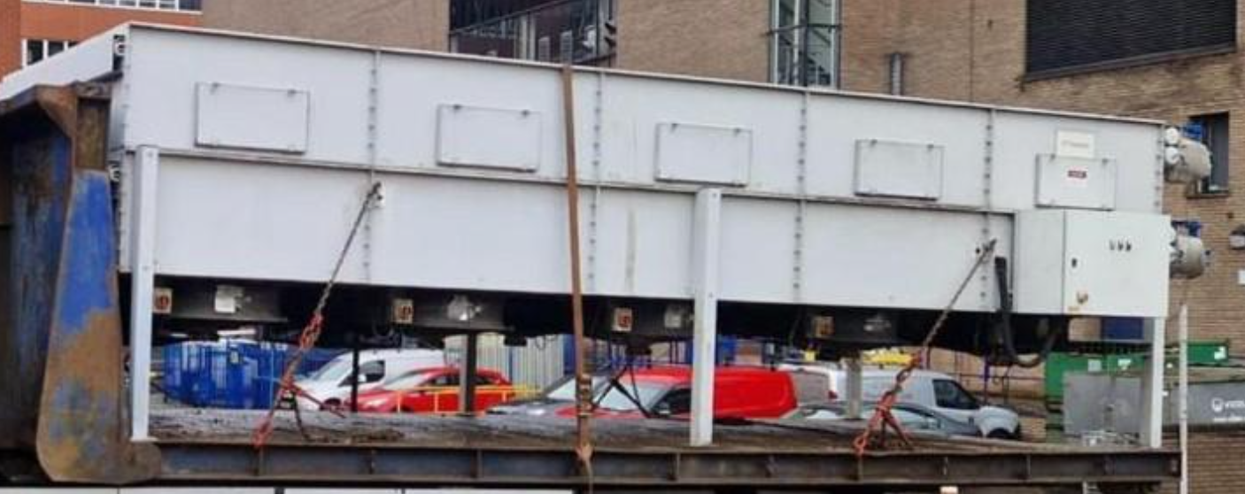 Image of a freight elevator moving between floors with several vehicles visible through its open sides.