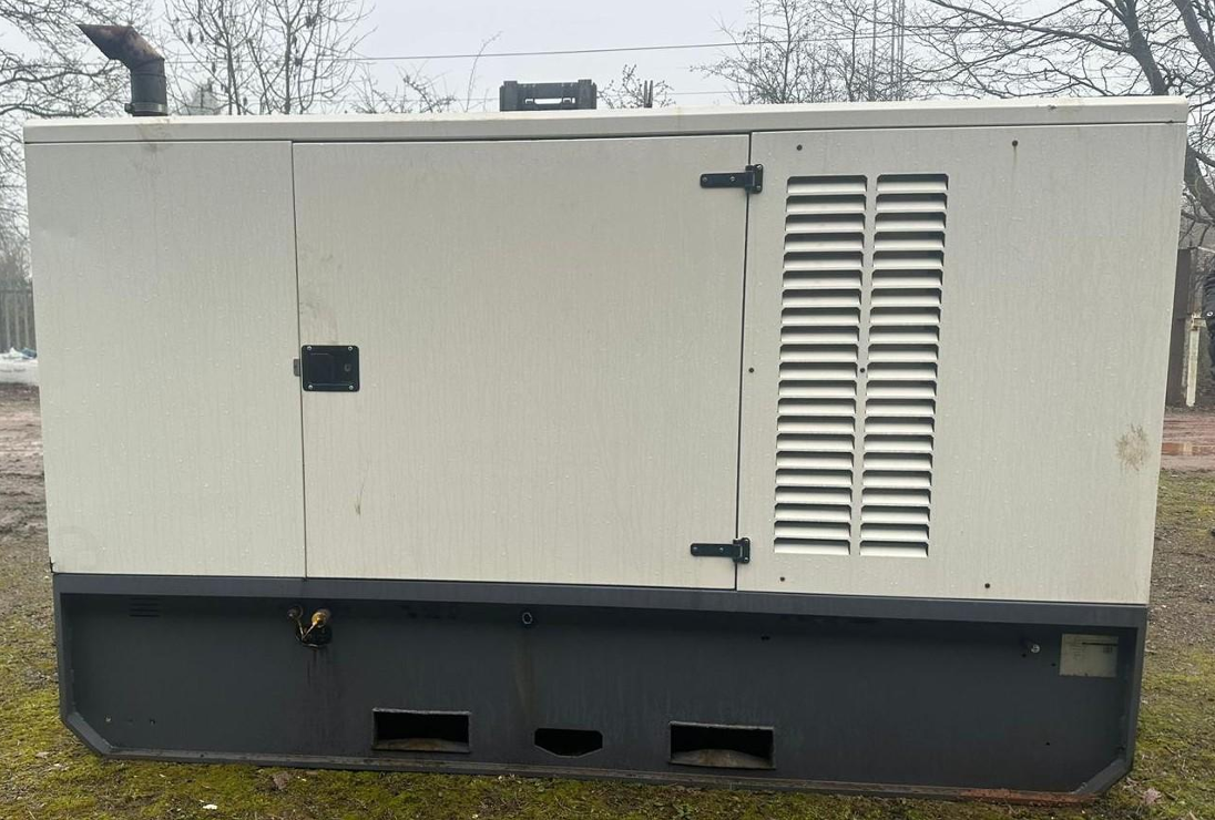 Large industrial generator box outdoors on grassy area with trees and power lines in background.