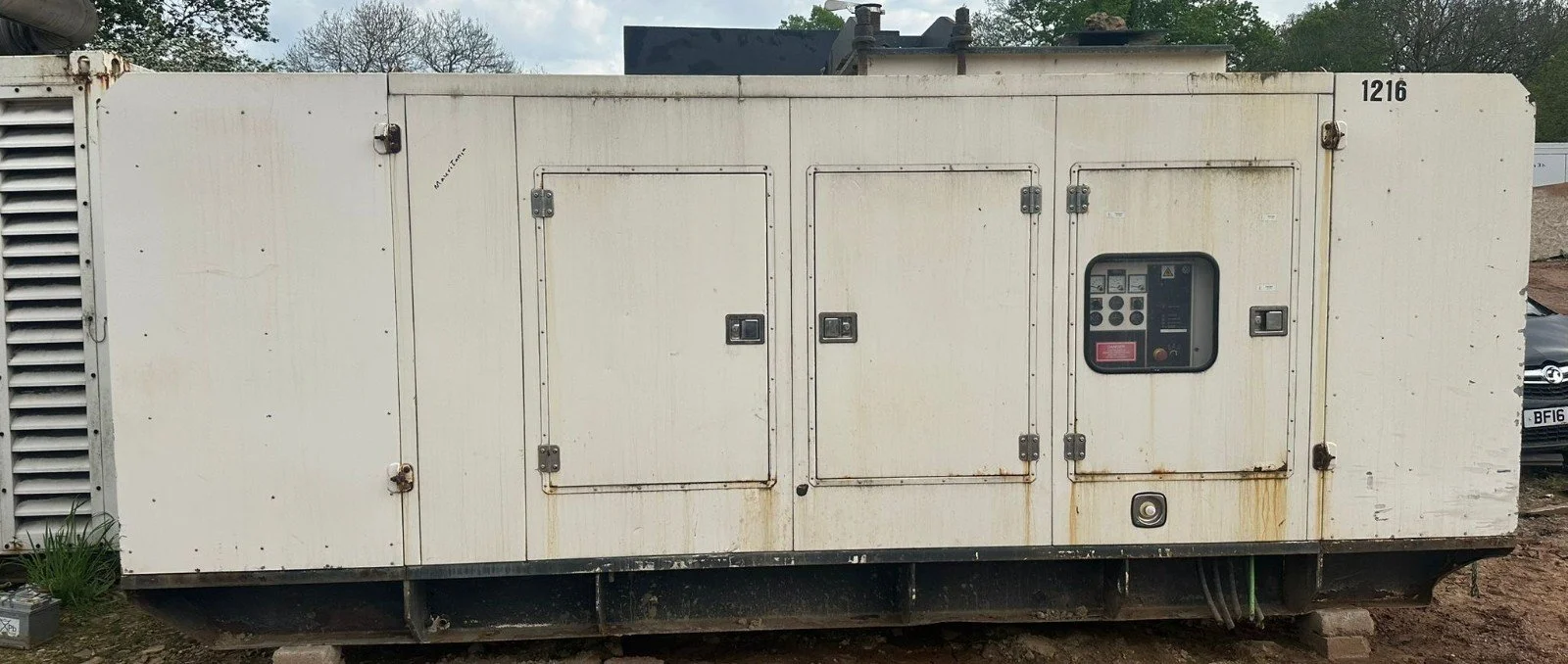 Large white industrial generator with control panel and access doors, placed outdoors on ground.
