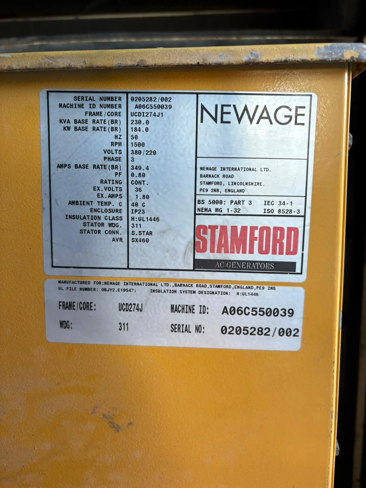 Close-up photo of a yellow industrial generator with informational labels, showing technical specifications and branding for Newage and Stamford.