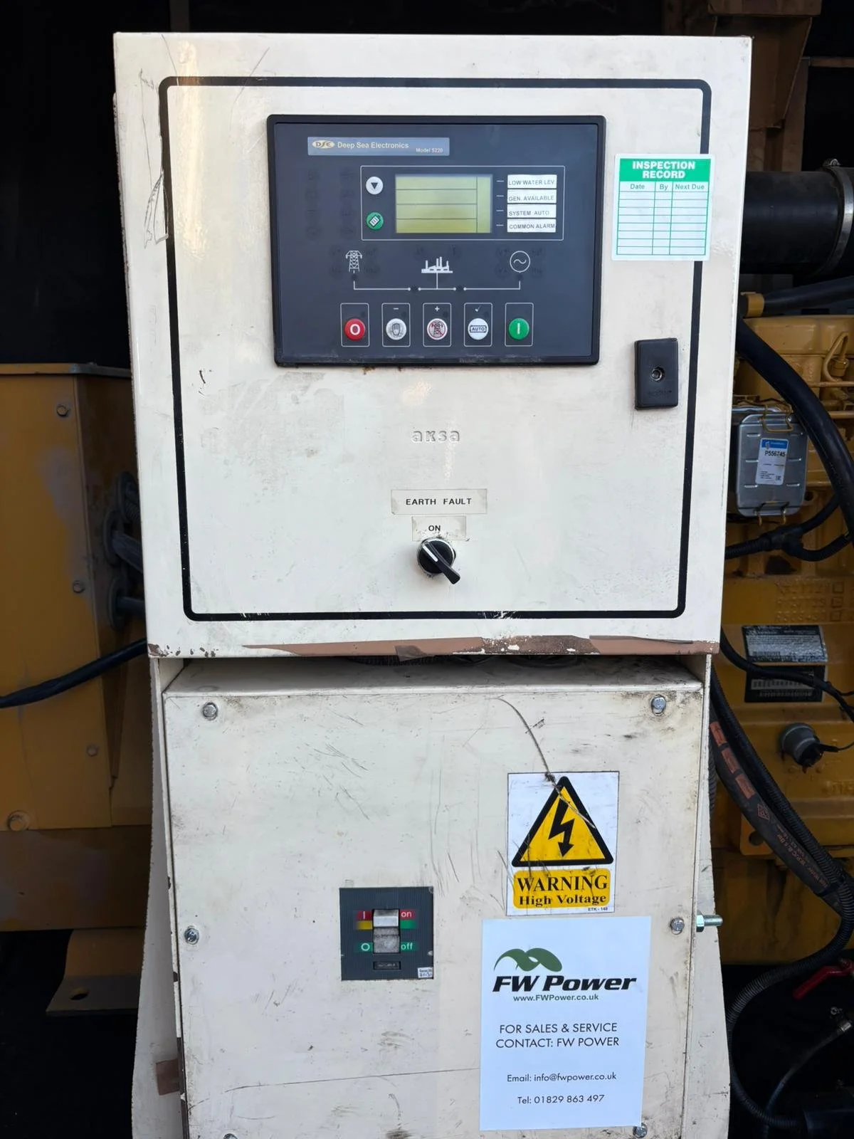 An electrical control panel with digital display, buttons, and an earth fault switch, mounted on a metal cabinet with warning labels and a service sticker.