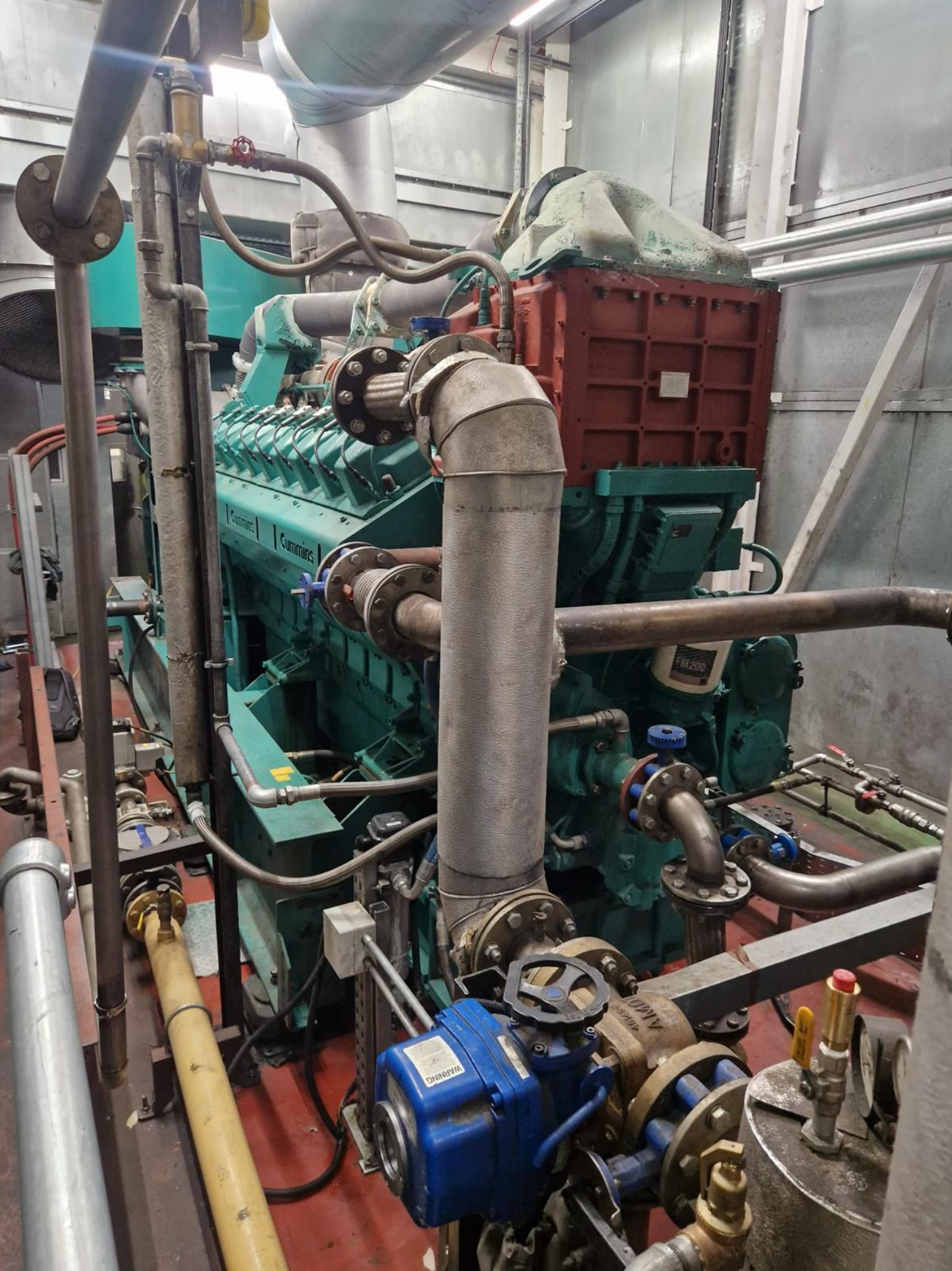 Industrial machinery with pipes, valves, and a large red and green pump in a mechanical room.